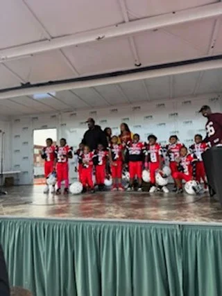Group of children in football uniforms standing on a stage with adults.