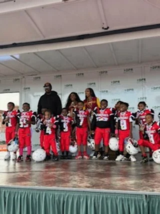 Children in football uniforms with coaches on a stage, some holding helmets.