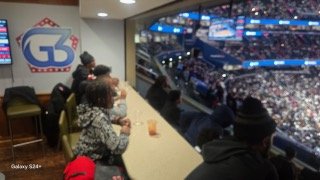 People watching a sports game at a stadium, sitting at a table inside a concession or VIP lounge.