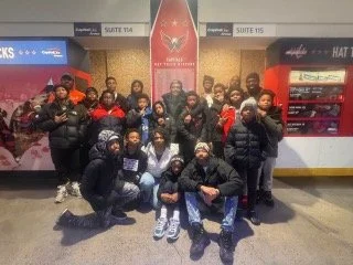 A group of people posing together outside a building with vending machines, some are holding red items, and they are dressed in casual winter clothing.