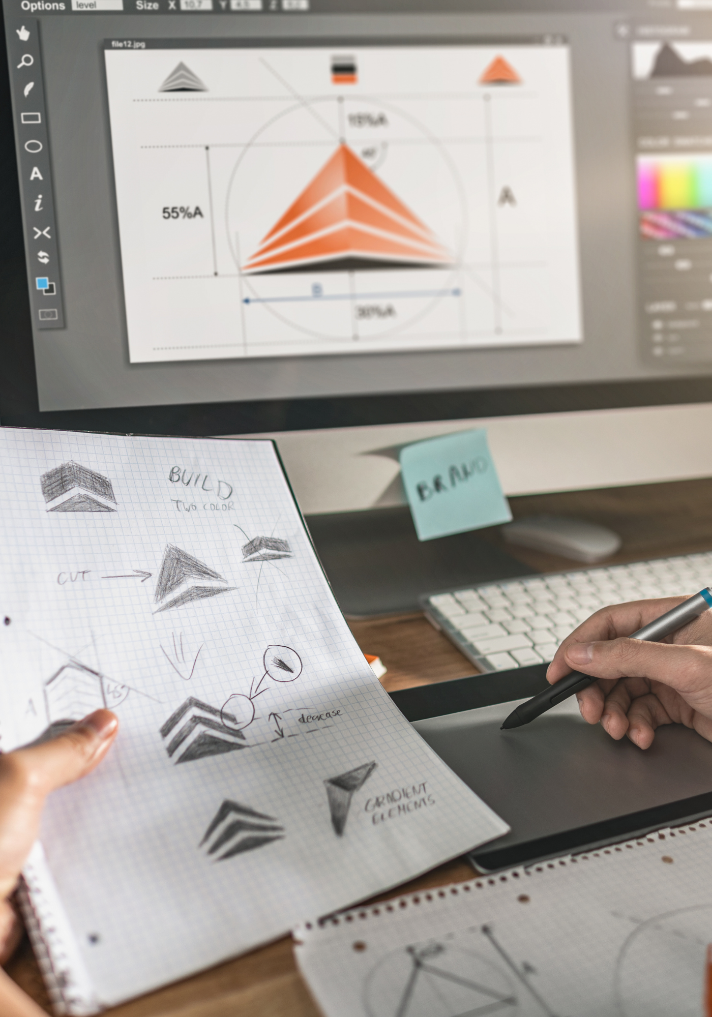 A person is working on illustrations and sketches of pyramids or triangles on graph paper, with a computer screen displaying a 3D diagram of triangular shapes and measurements.