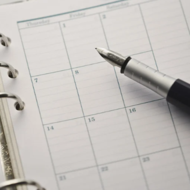 Close-up of a planner or calendar with a pen resting on it.