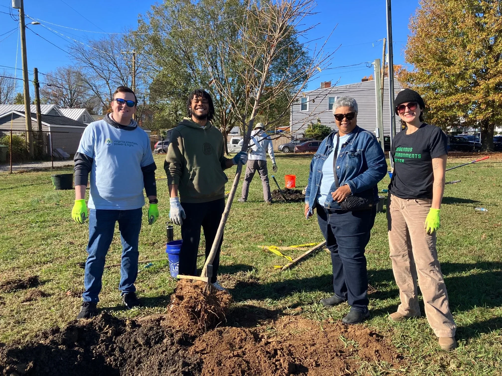 Four staff members from Virginia Interfaith Power & Light posing with a young tree they are in the process of planting.