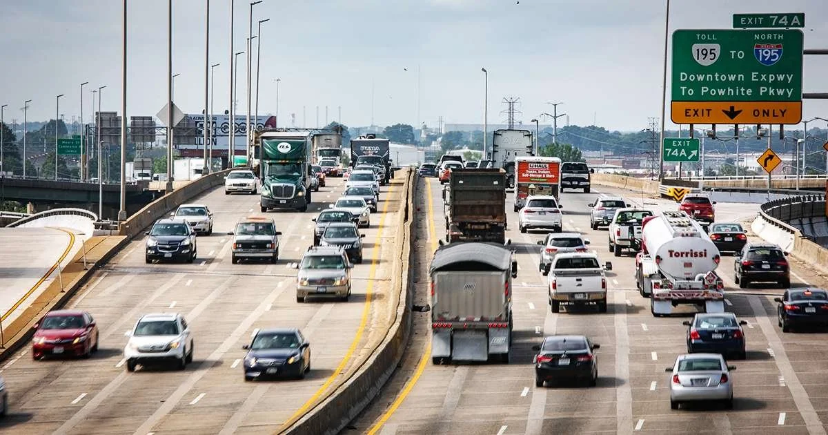 Cars and semi trucks drive north and south on Interstate 95 on a sunny, shadeless day.