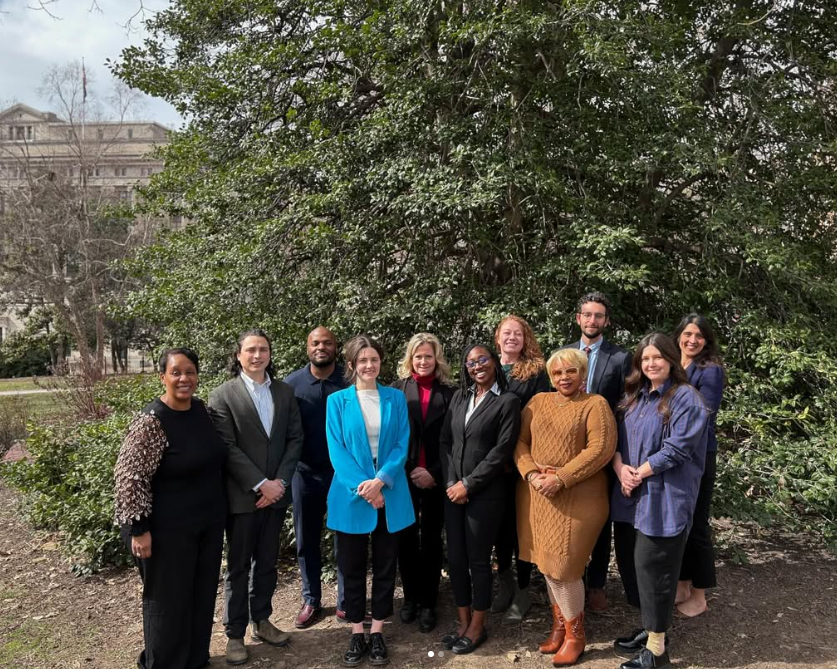 Team photo of the Office of Sustainability team standing in front of a stand of trees and shrubs.