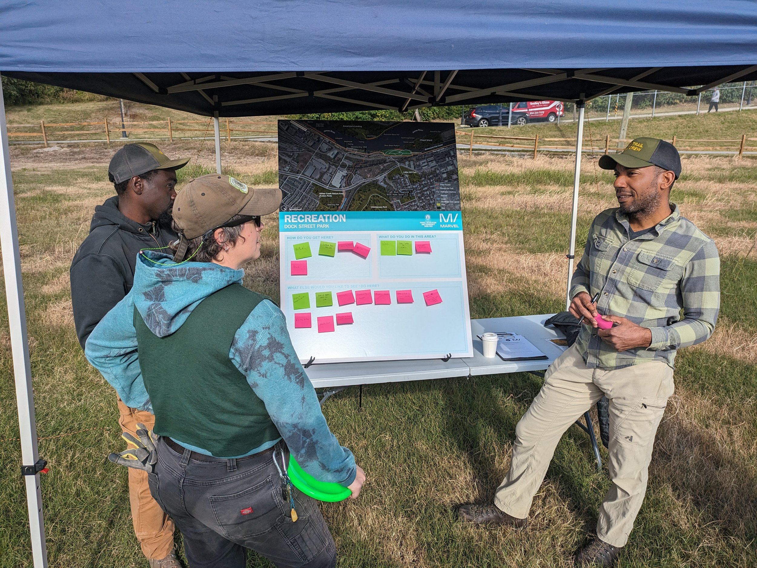 Andrew Alli, the Superintendent of the James River Park System, talks with community members in front of a tabling booth at a community event for the Richmond Tree Plan.