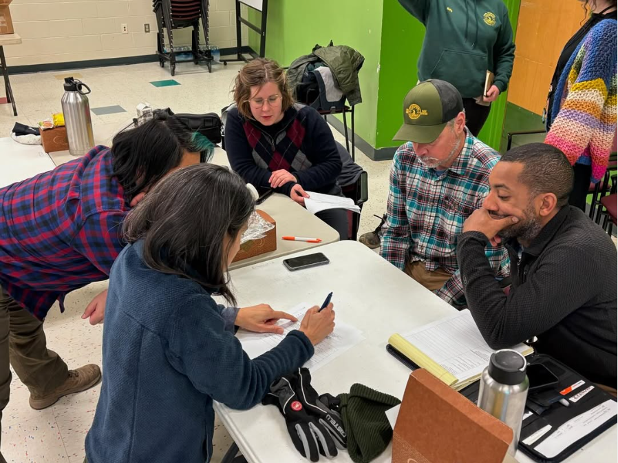 A group of five City staffers gather around a table in discussion while one member writes on a piece of paper.
