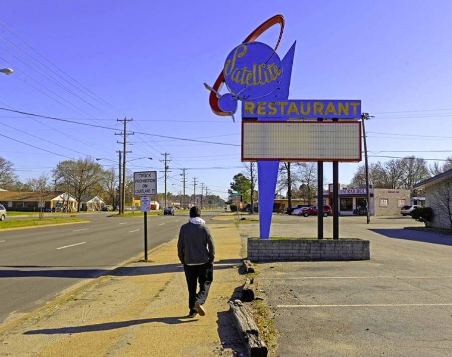 A person walks on a sunny sidewalk without any nearby trees near the Satellite Restaurant in Richmond.