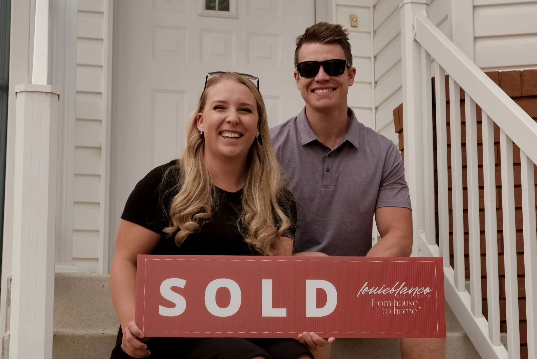 Happy couple sitting on front porch stairs holding a red 