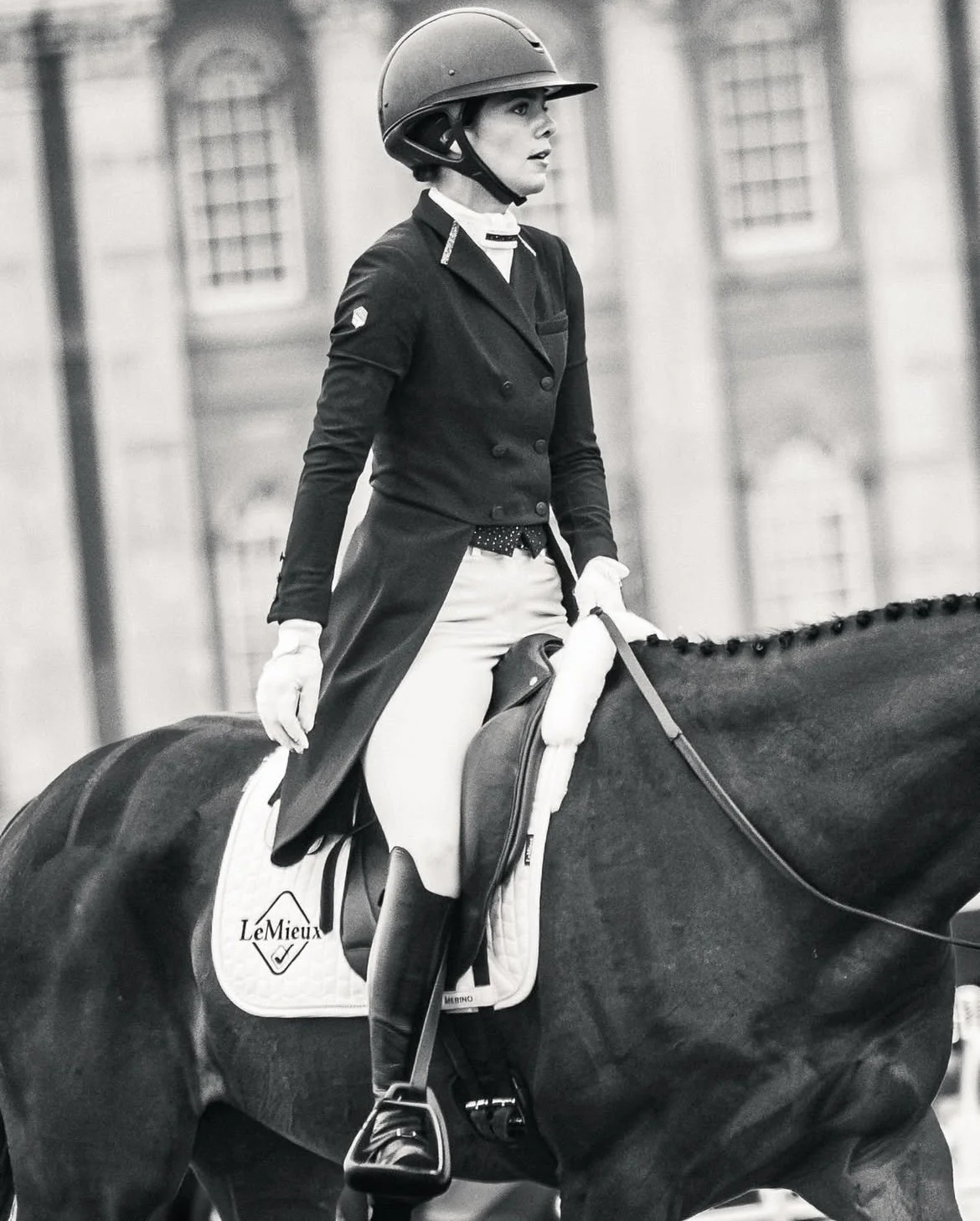 A woman riding a horse in equestrian attire, wearing a helmet and riding jacket, in black and white.