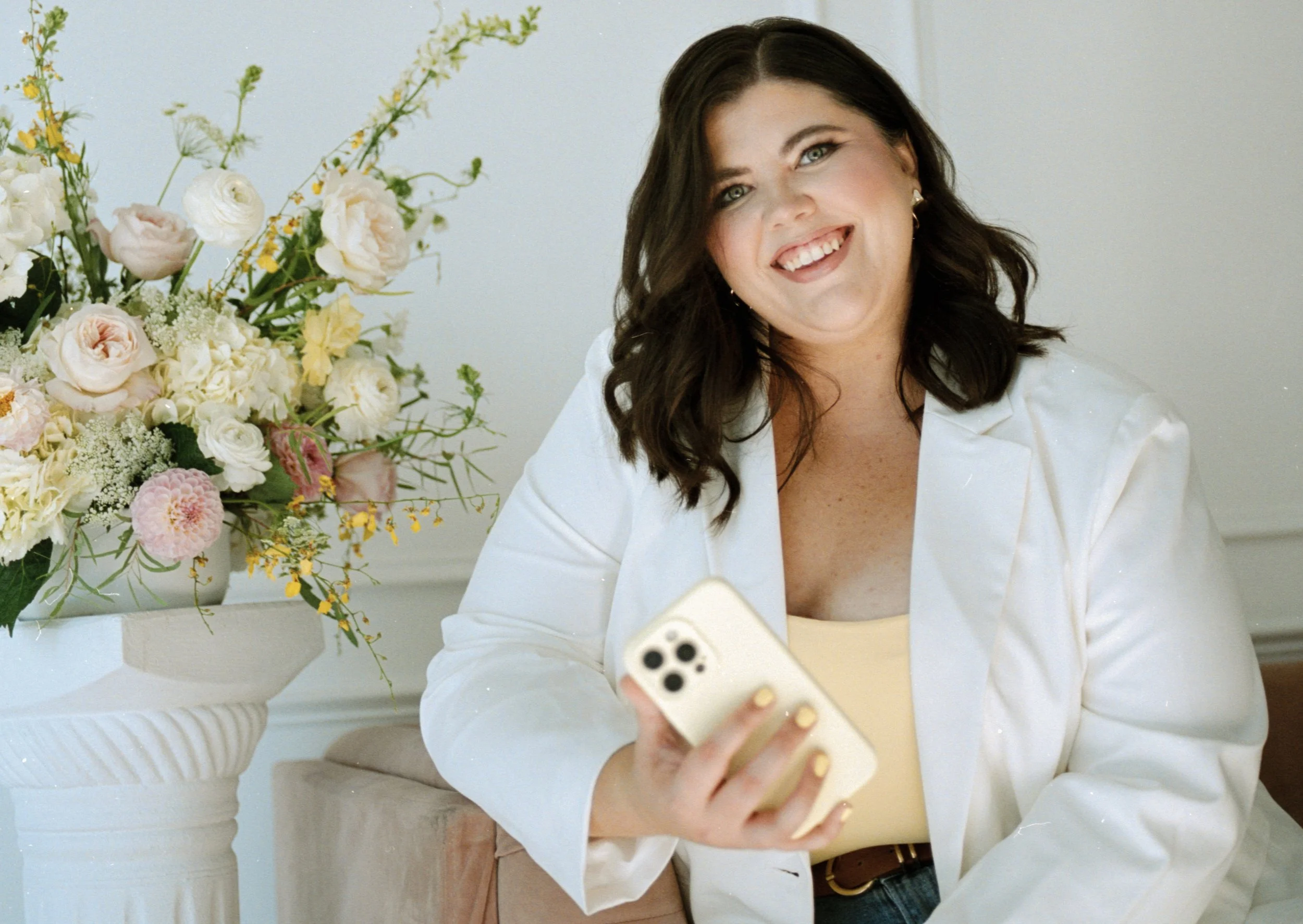 Dallas wedding content creator Cheyenne Allgood smiling while holding an iPhone in a light-filled studio setting