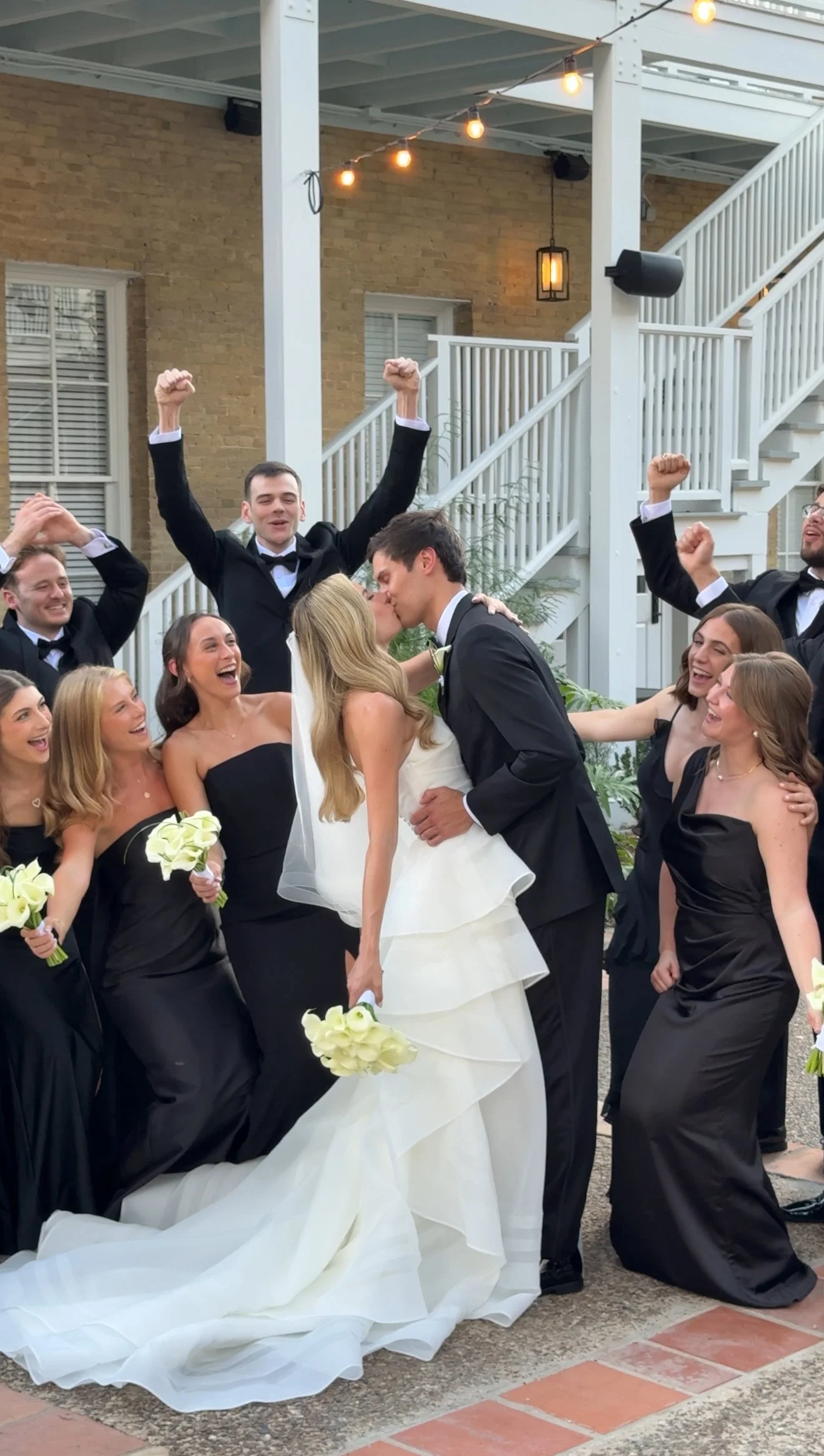 Bride and groom kissing surrounded by their wedding party during a lively outdoor wedding moment captured by a wedding content creator.