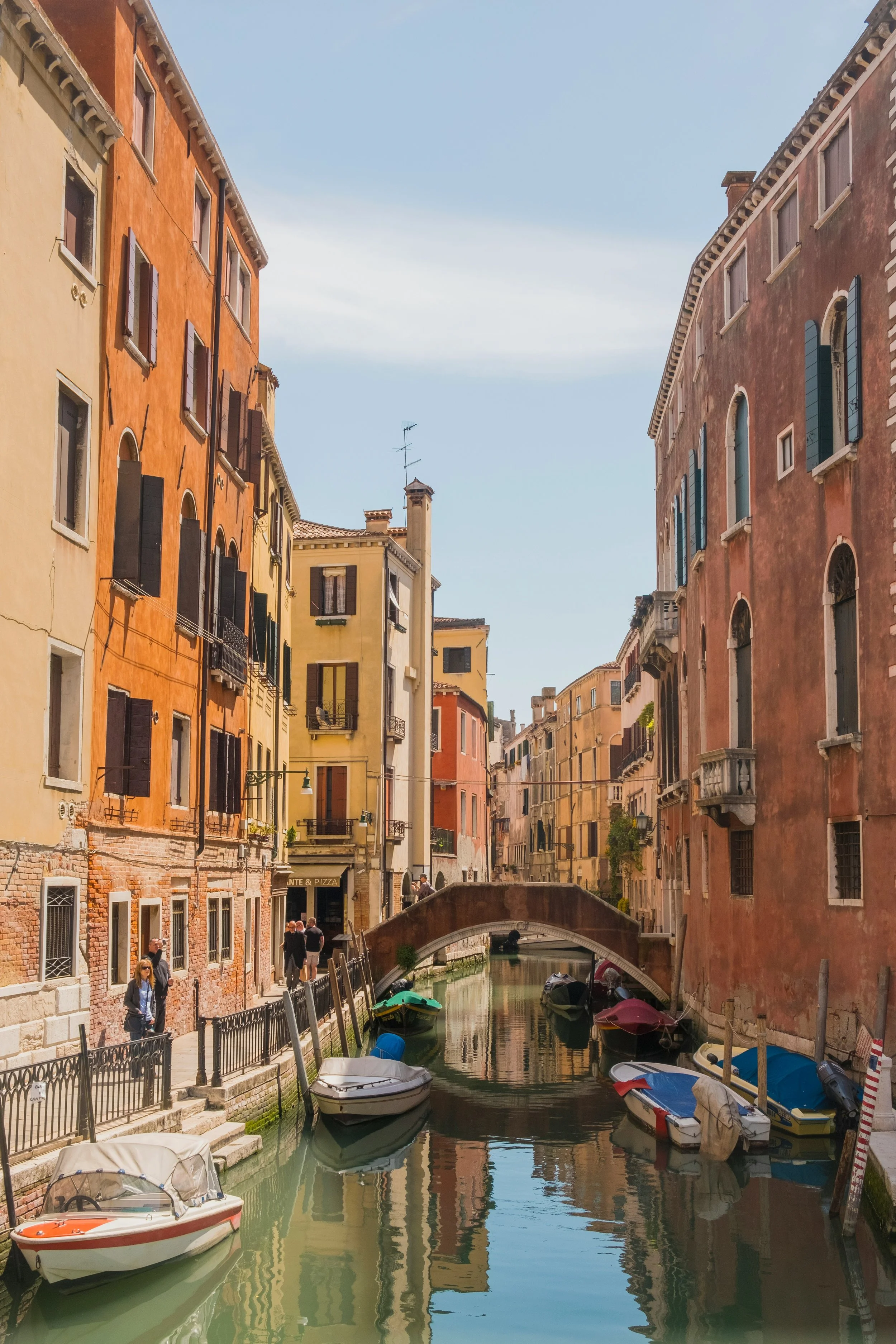 Colorful buildings lining a canal with boats and a small stone bridge in Venice, Italy.