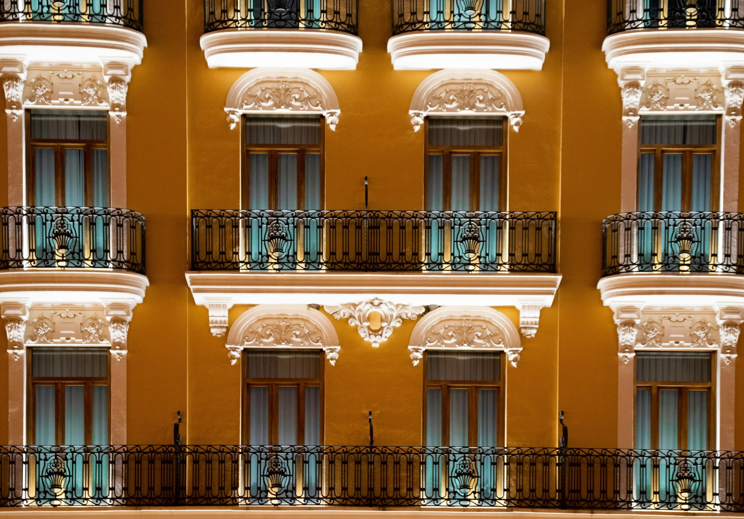Multiple historic-style balconies with ornate white trim on a yellow building at night.