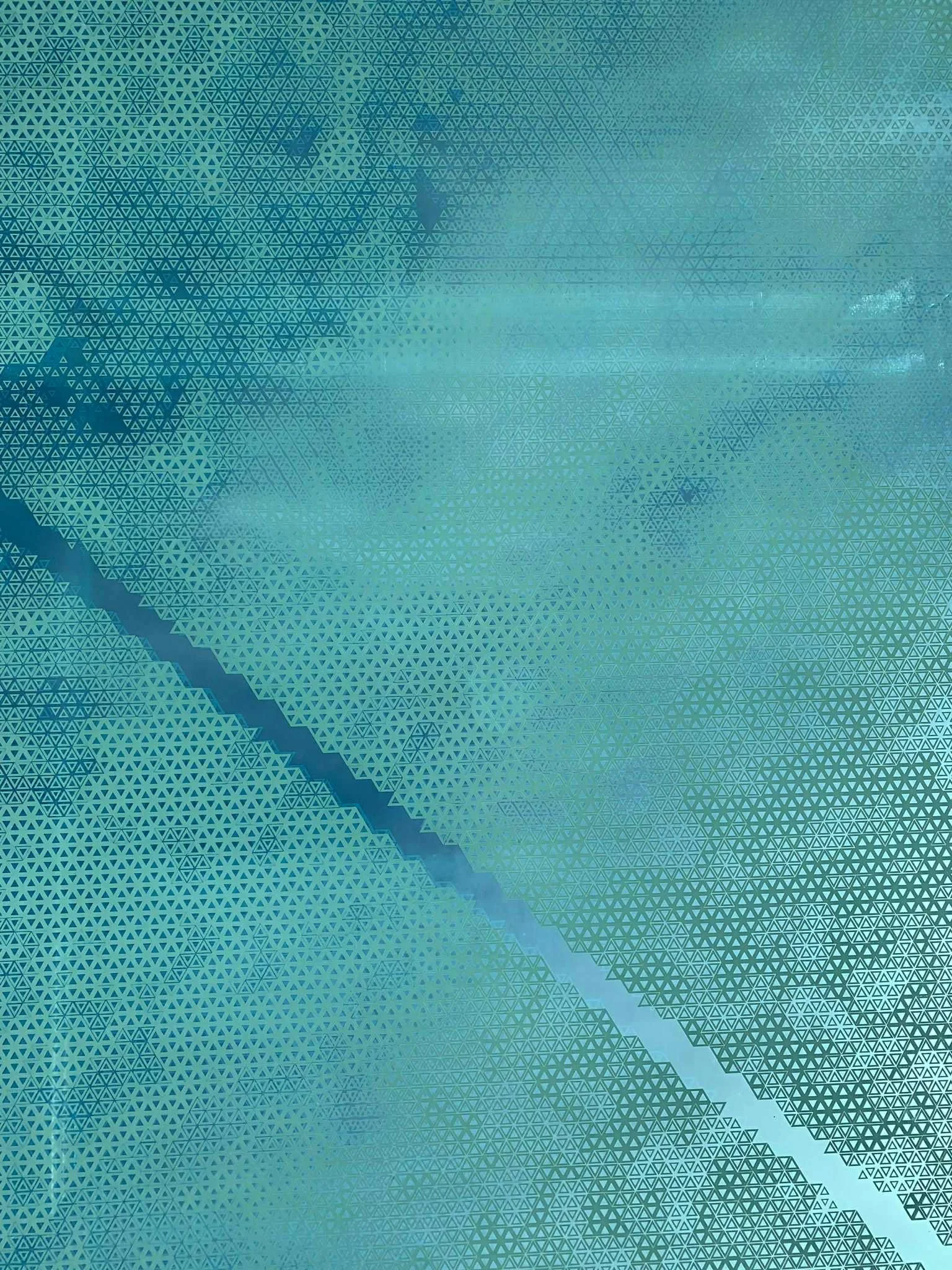 Abstract geometric pattern with teal, green, and blue shades, featuring small and large triangles arranged in a wave-like pattern.