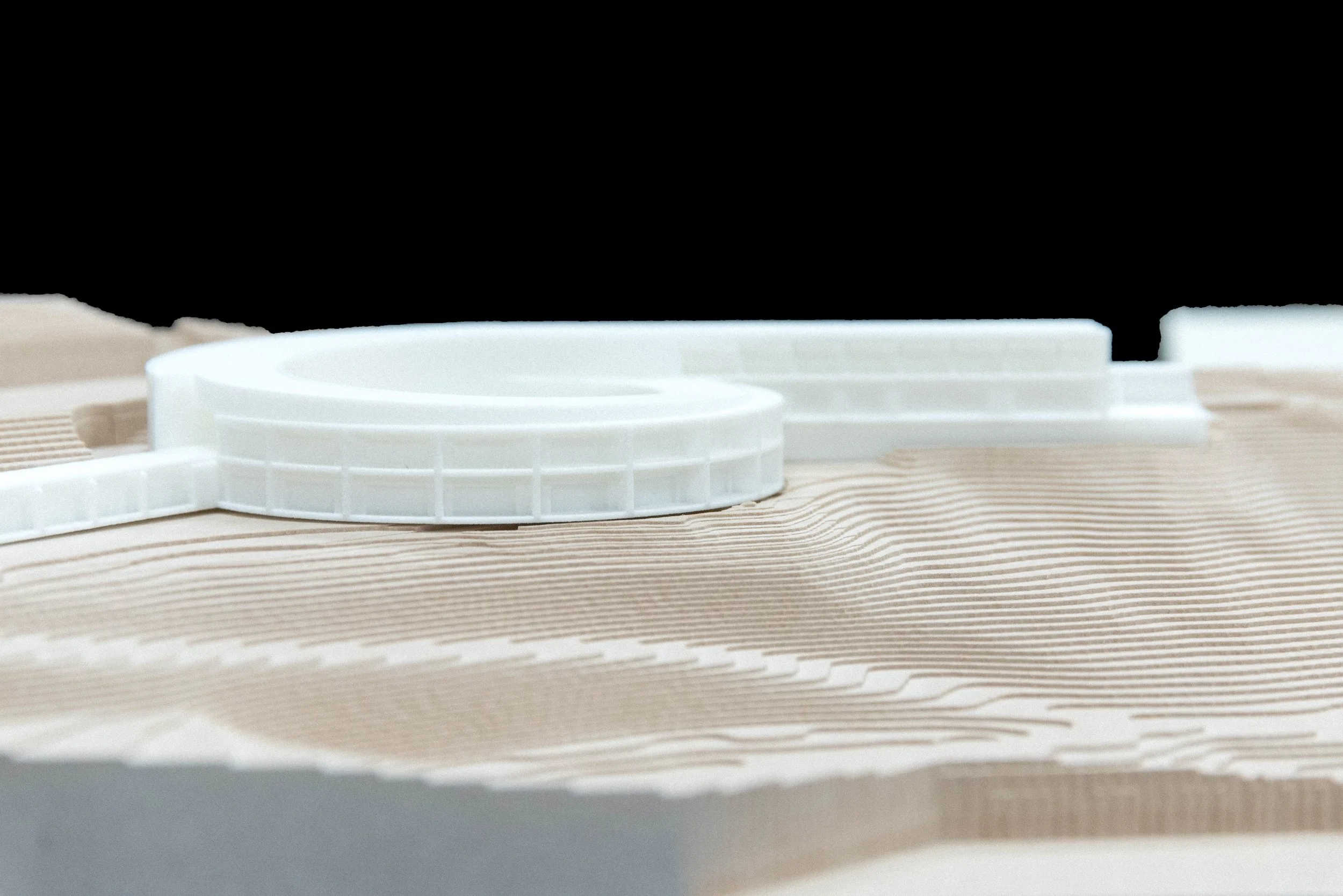 Architectural model showing a curved white structure on a layered terrain model.