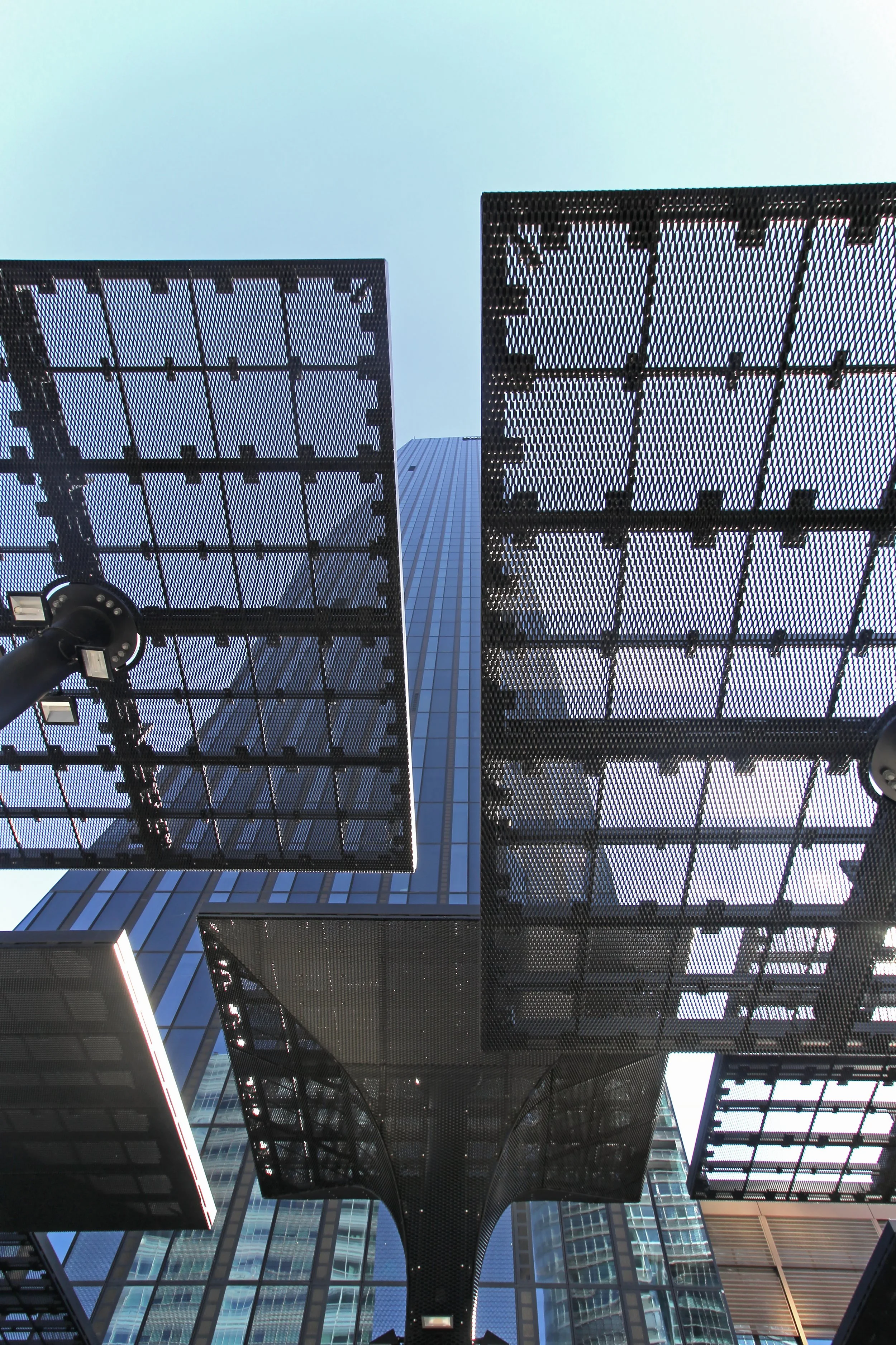 Low-angle view of a modern building with solar panel canopies and a tall skyscraper in the background.