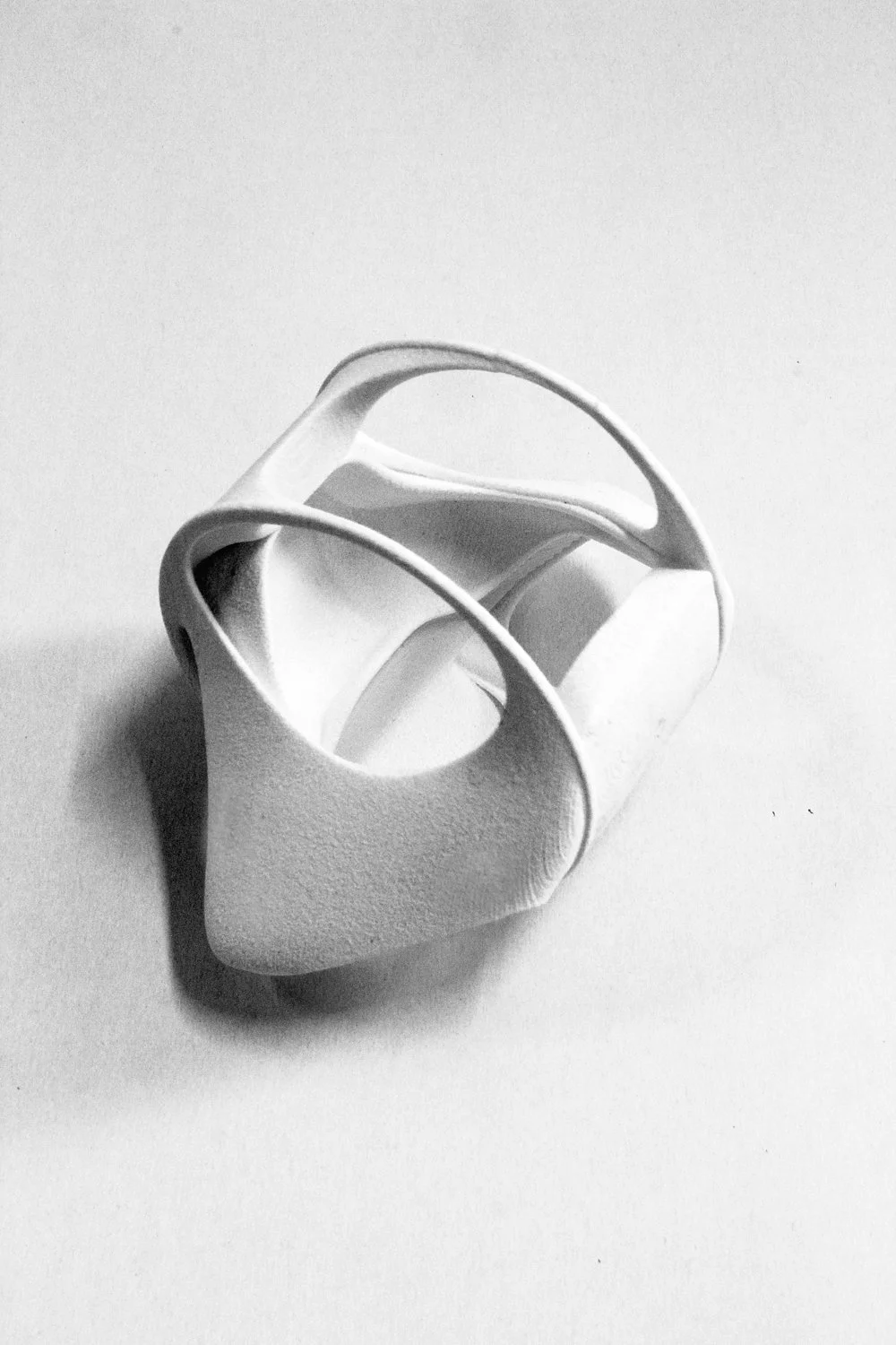 A white 3D-printed object with an abstract, spiral, and skeletal design is placed on a white surface with a subtle shadow.