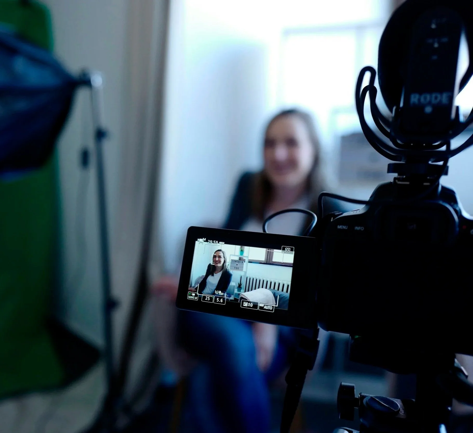 Camera viewfinder screen showing a woman smiling in a well-lit room with a window in the background, with various camera settings displayed.