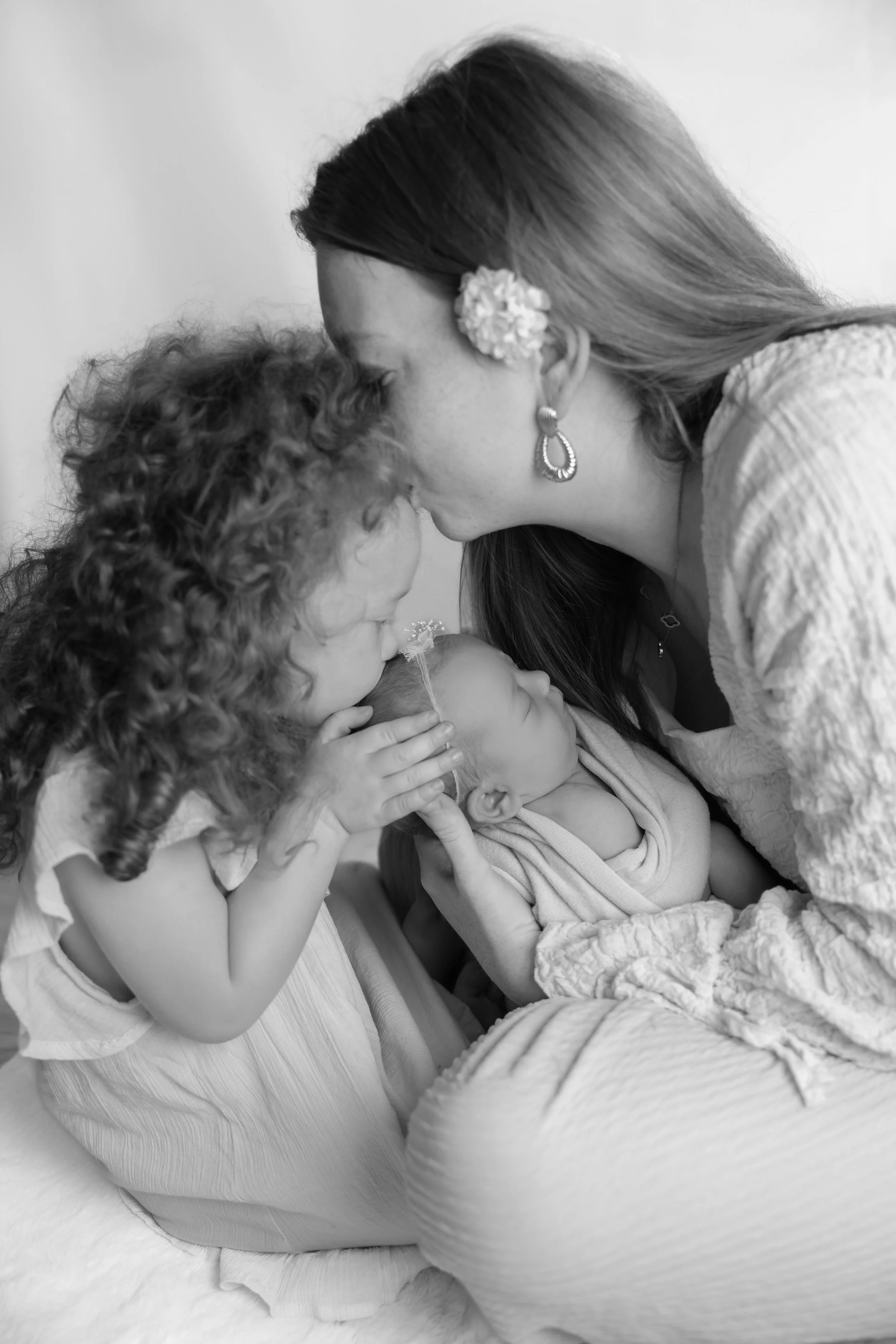 Une femme et deux jeunes enfants, une fille et un bébé, se font un câlin et un baiser, dans un contexte familial et tendre.