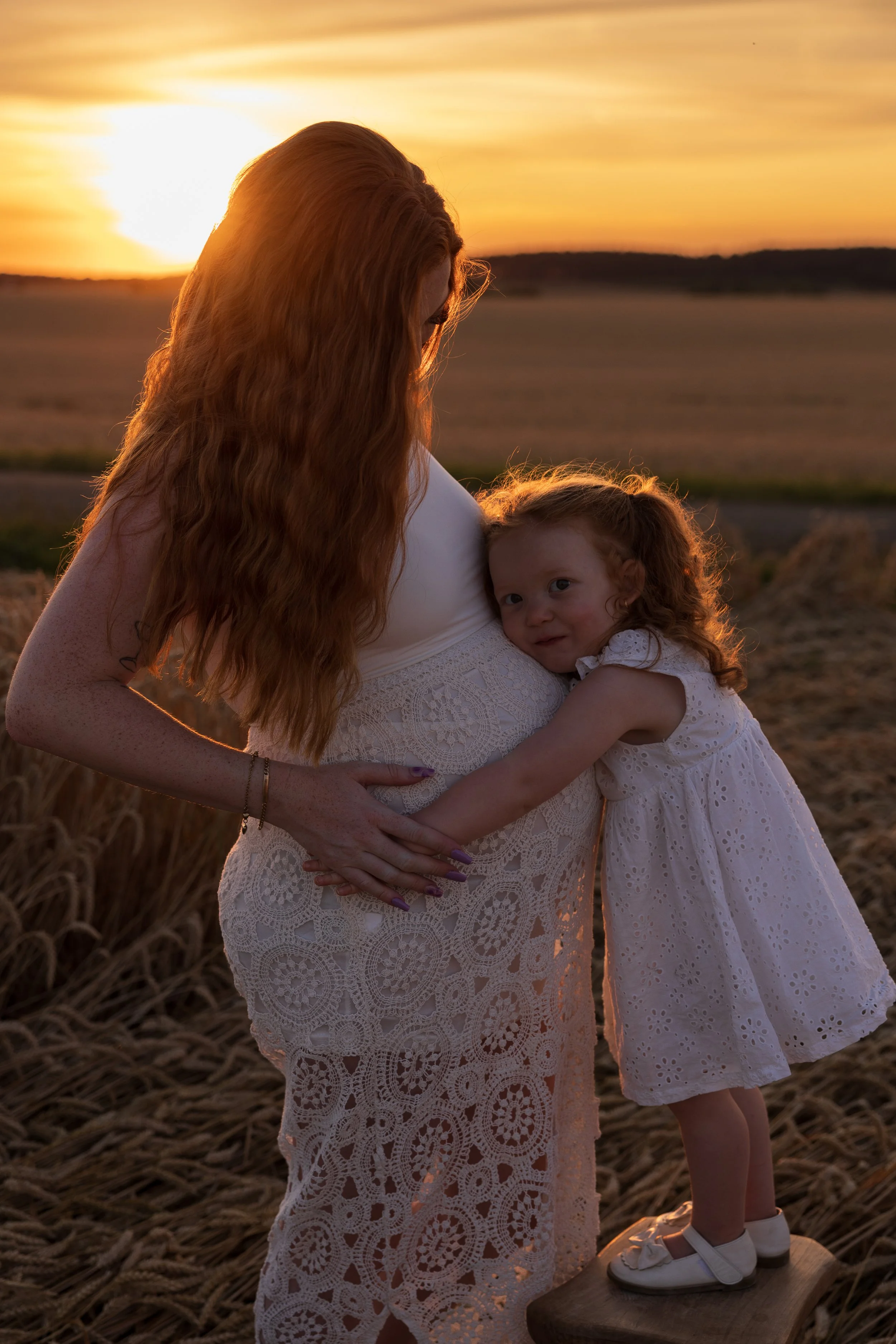Une femme enceinte avec une fille, dans un champ au coucher du soleil.