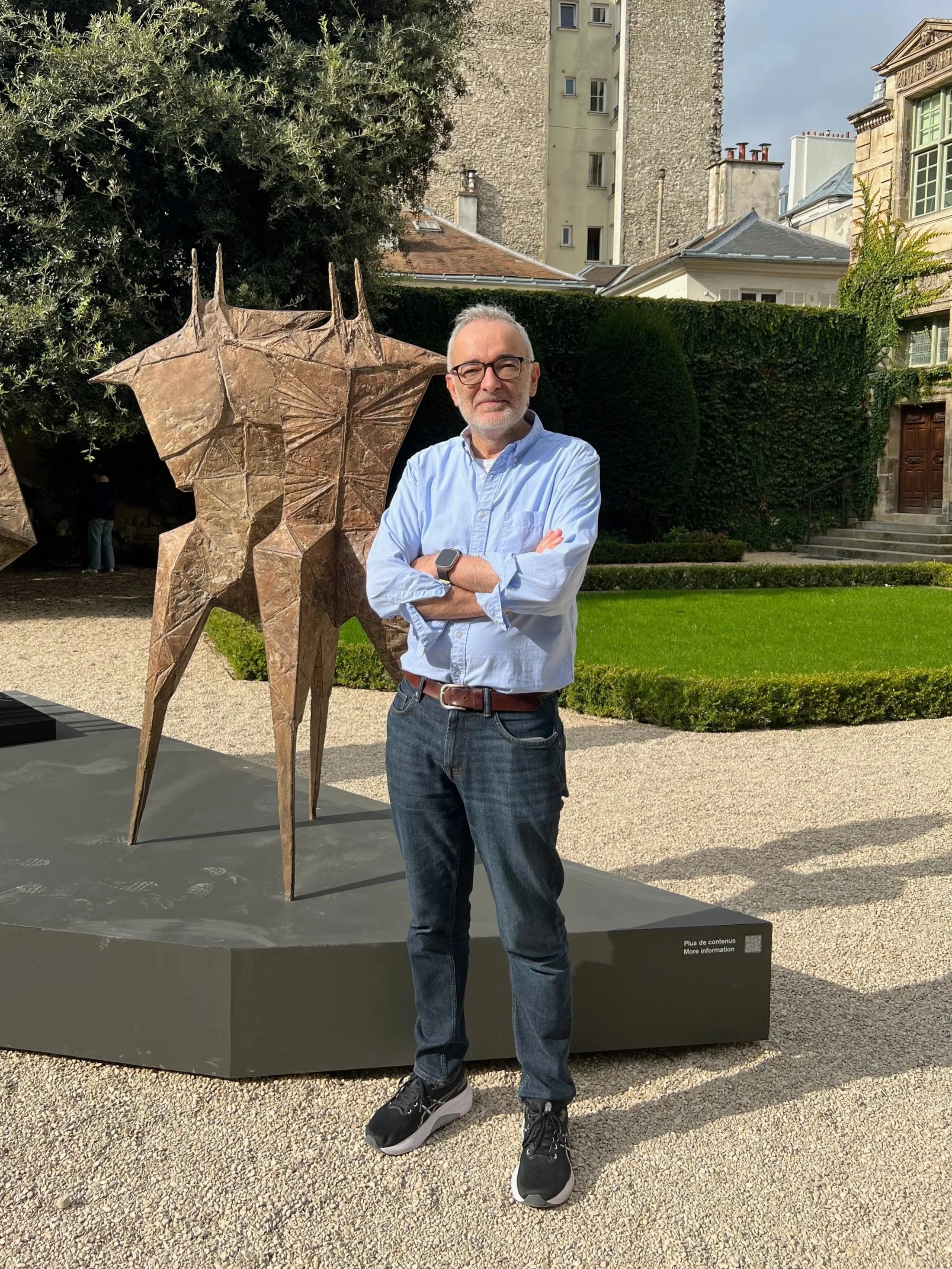Joe Madeira standing next to a bronze sculpture by Lynn Chadwick in an outdoor courtyard garden.