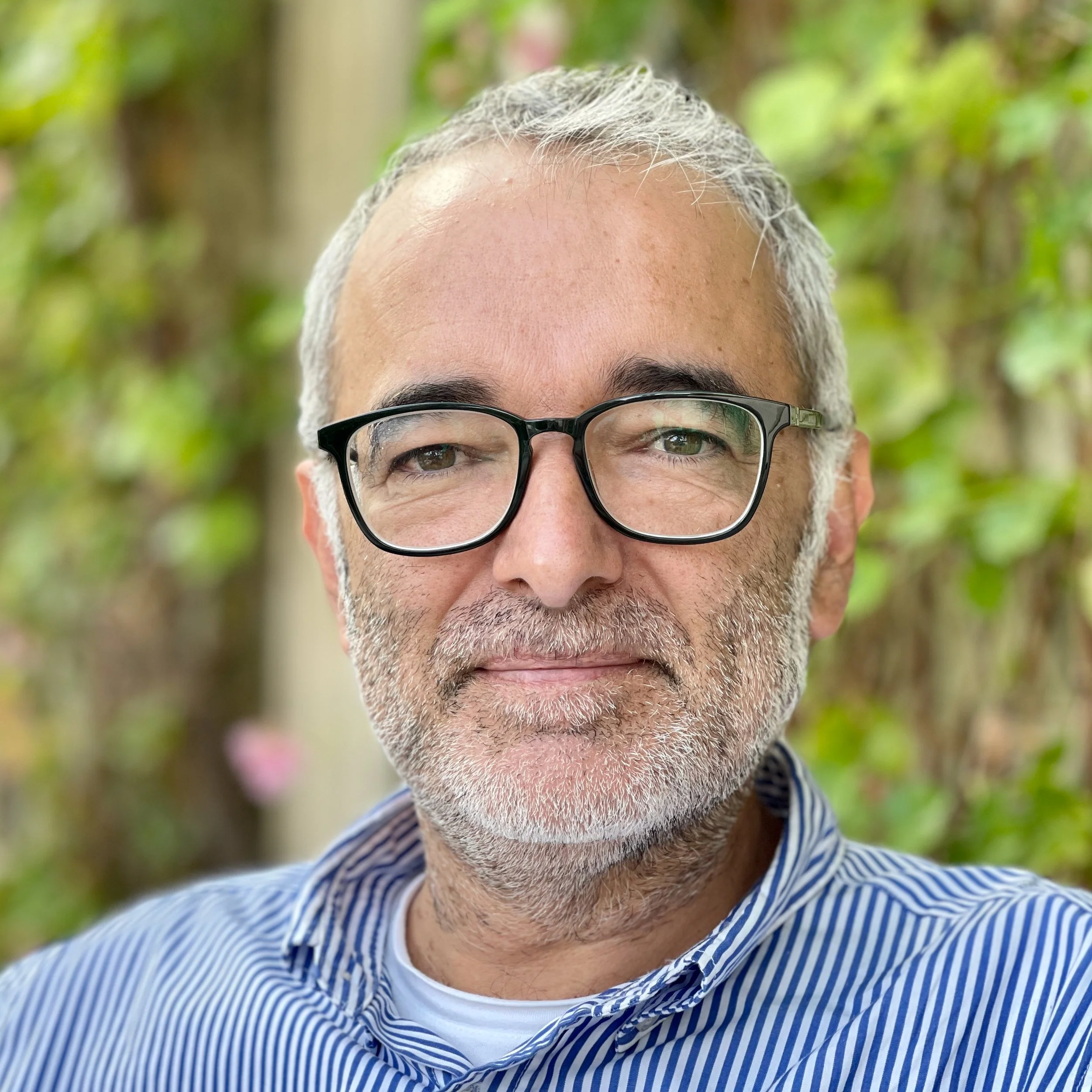 Portrait of Joe Madeira, Artlogic Specialist and artist, wearing glasses and a striped shirt.