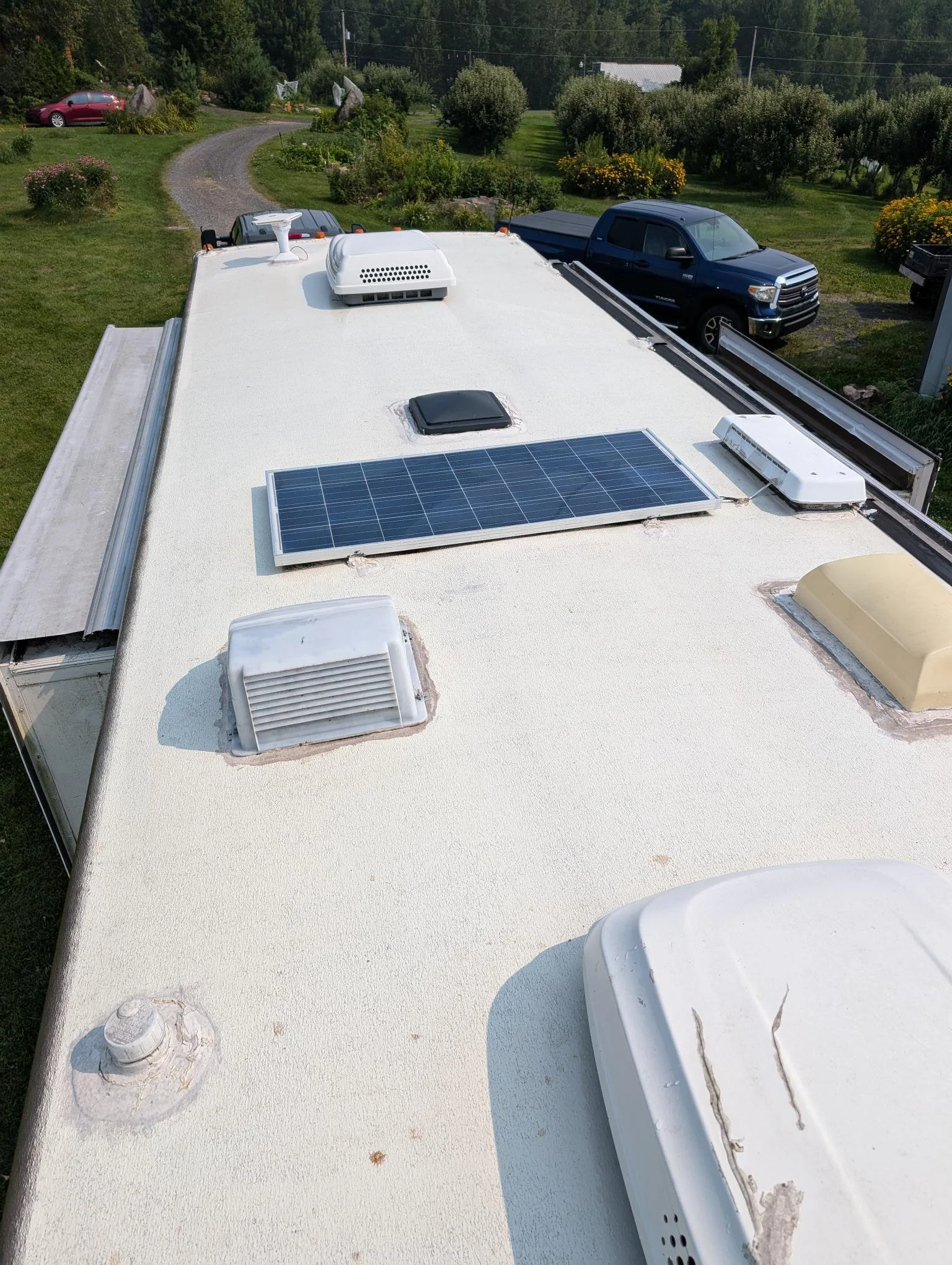 Toit d'une caravane avec des panneaux solaires, ventilations et autres équipements, dans un environnement verdoyant.
