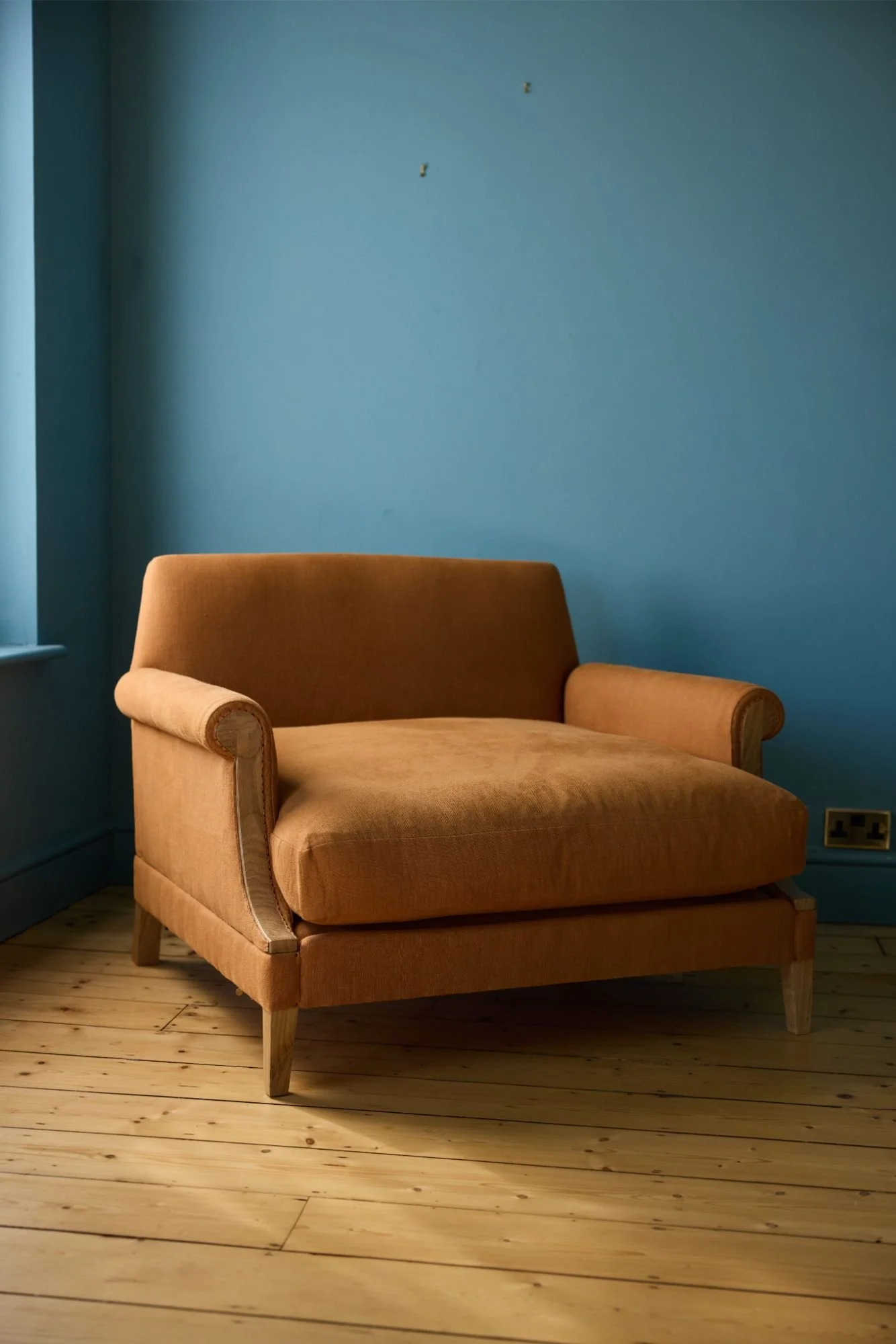 A large bespoke armchair 'The Aldan' by furniture designer and maker Trew and Bold, covered in orange linen photographed on a soft blue room