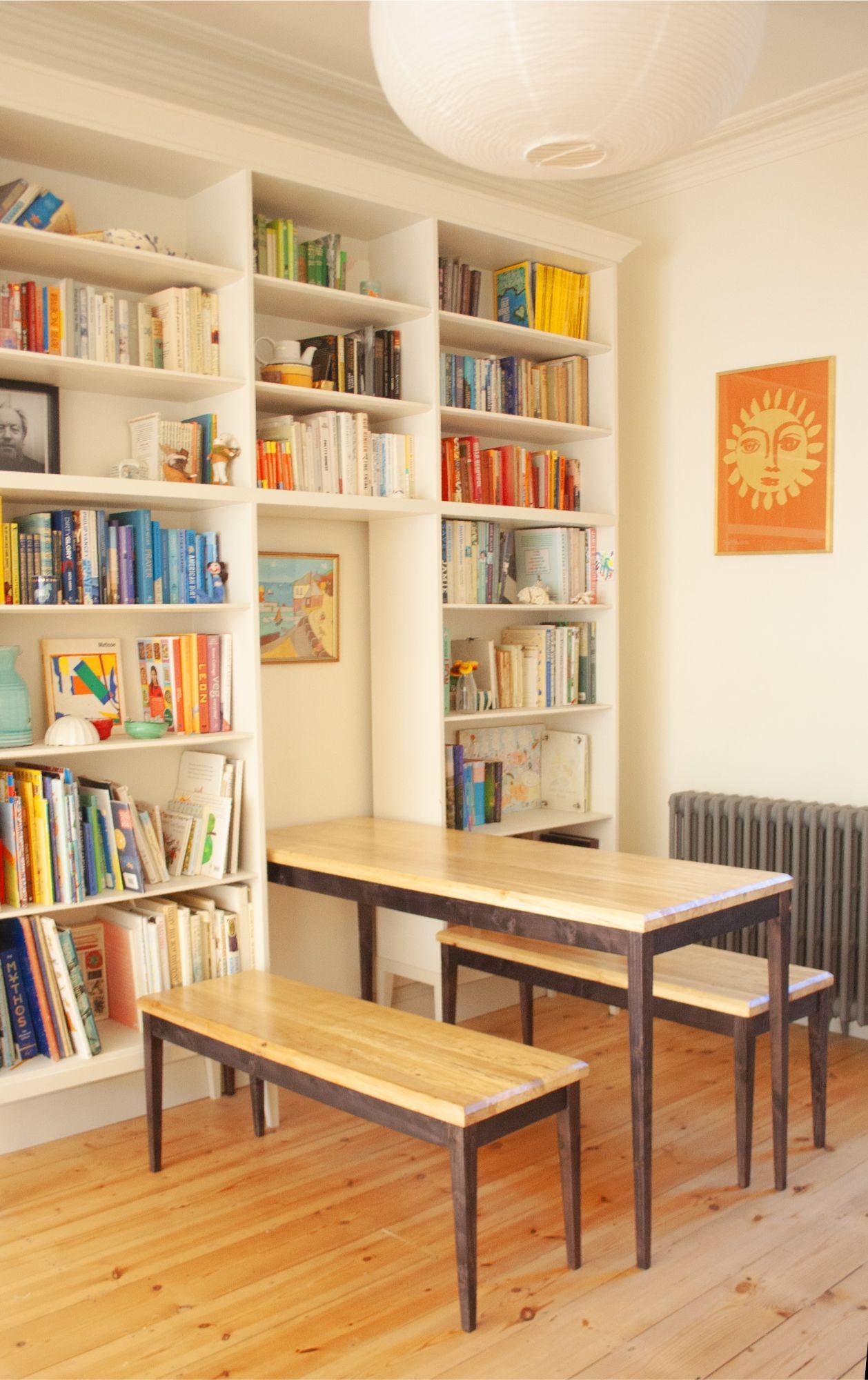 The Calder table and Benches in a bright room with a wall of colourful books. Designed and made for this home by Trew and Bold in their workshop in between Bristol and Bath near the Cotswolds