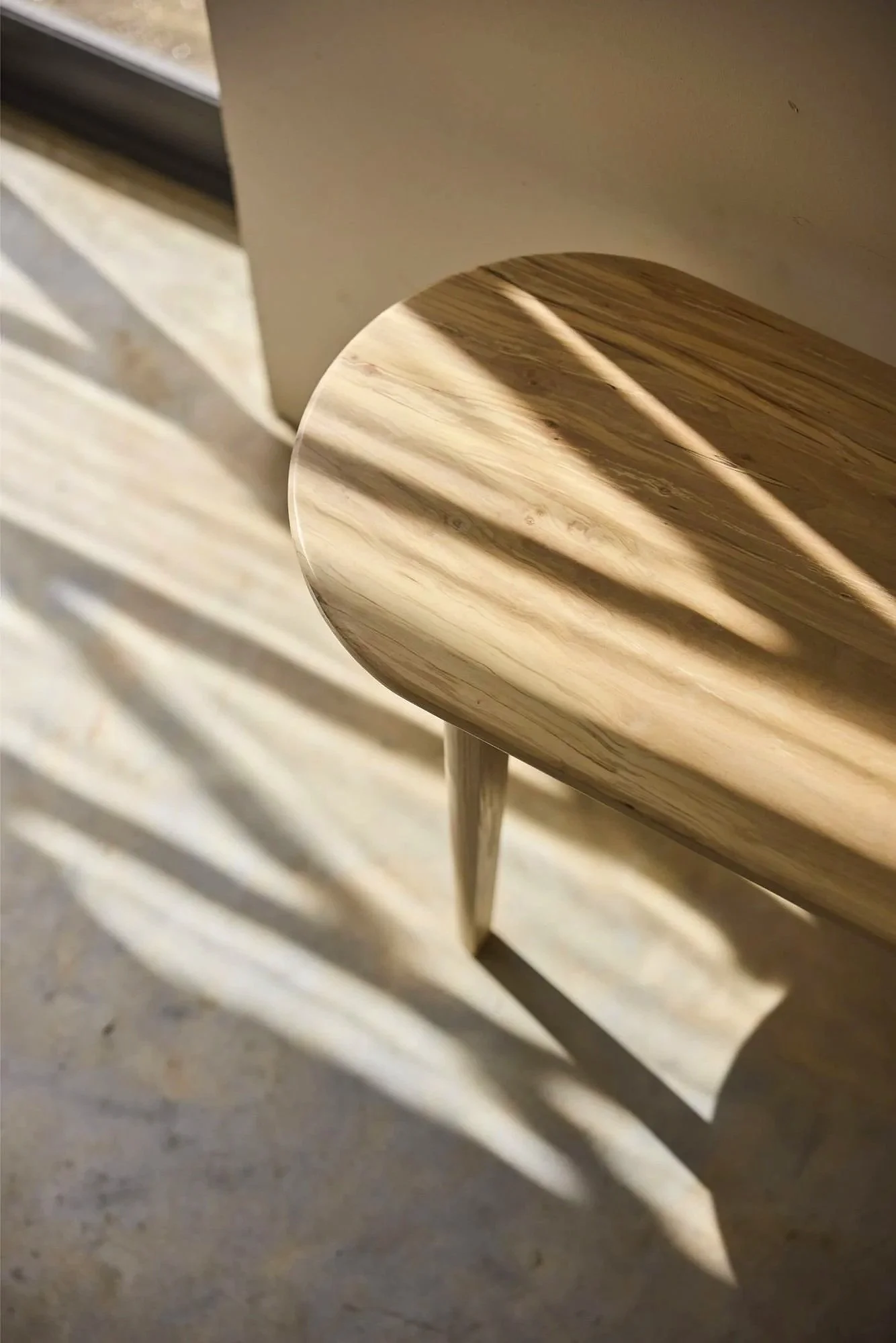 Close-up of a wooden bench handmade near the cotswolds with shadows cast by nearby objects creating an abstract pattern on the surface.