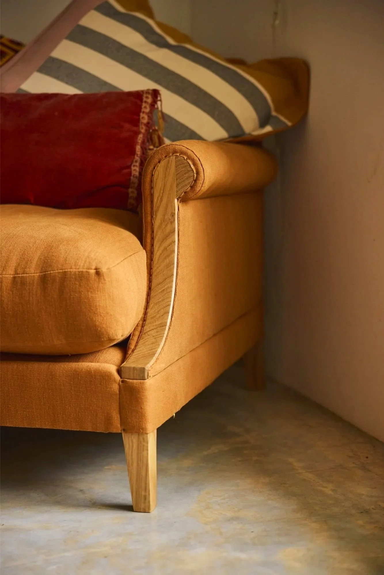 Detail of a large loveseat designed and made to order by Trew and Bold a furniture workshop near Bristol. This chair is made with a solid oak frame and traditionally upholstered with Orange linen fabric