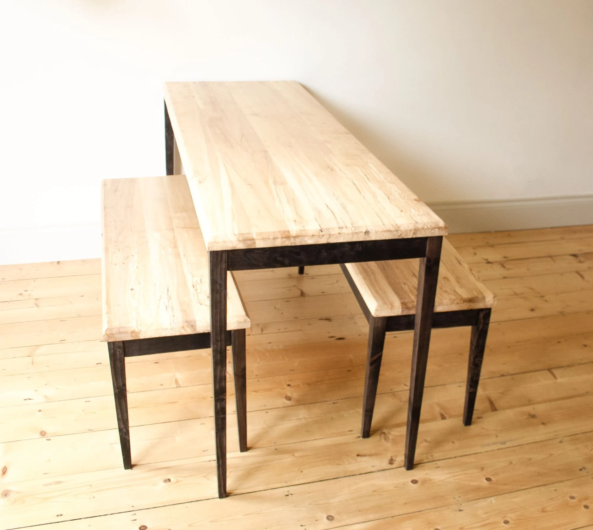 a table and benches set made from spalted silver birch tops with stained ash leg frames in a pale minimalist room with a wooden floor