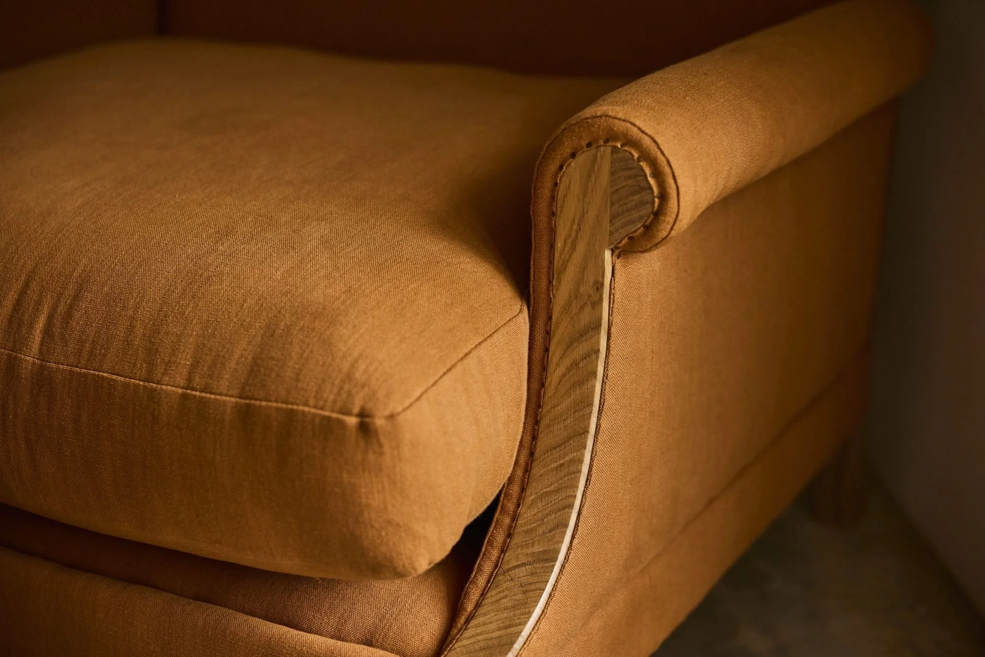Close-up of The Aldan Loveseat arm in an orange linen paired with the solid oak frame. Trew & Bold uses all British Timber