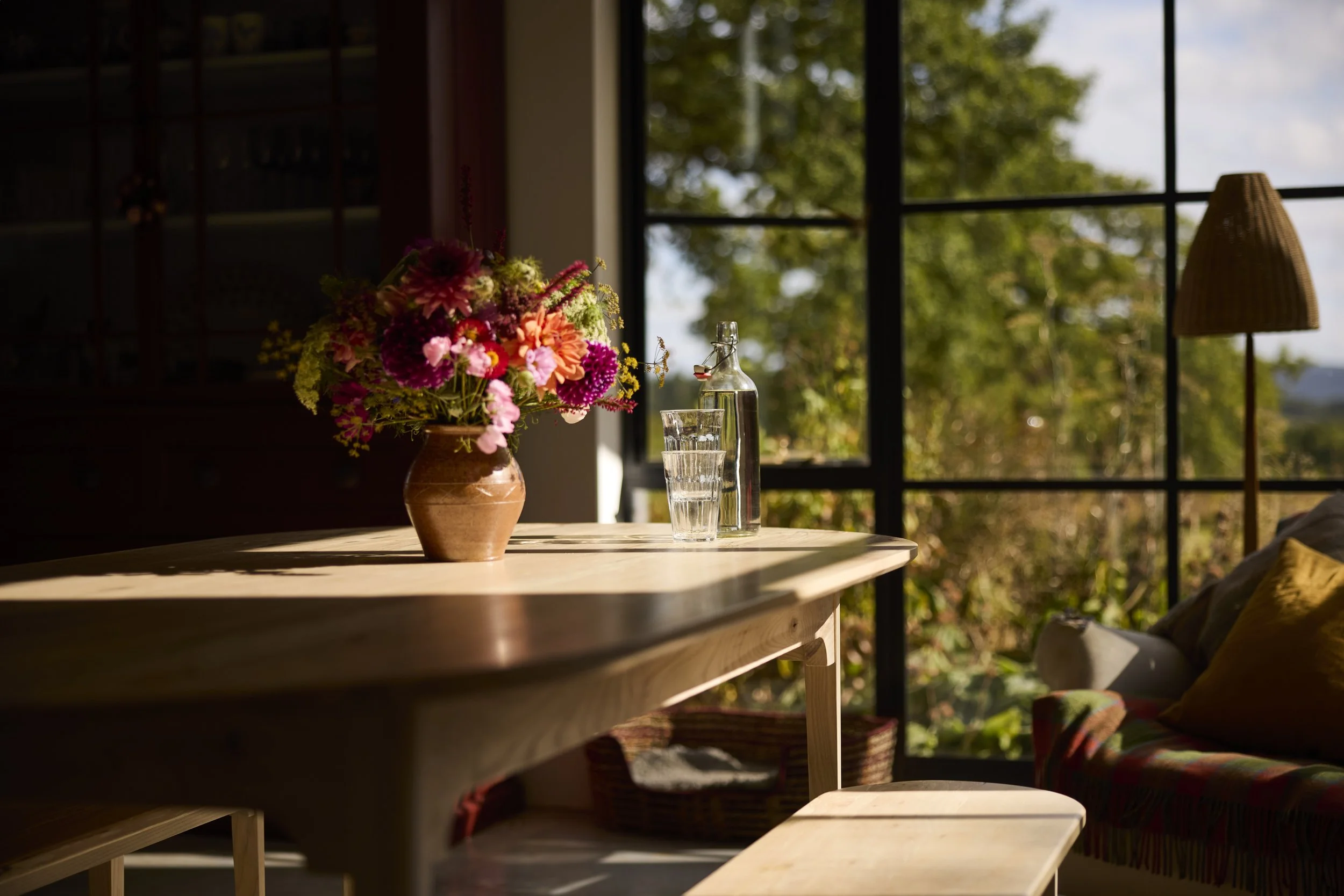 A dramatic shot of handmade solid dining set in bright sunlight with warm shadows and colourful flowers on the table top