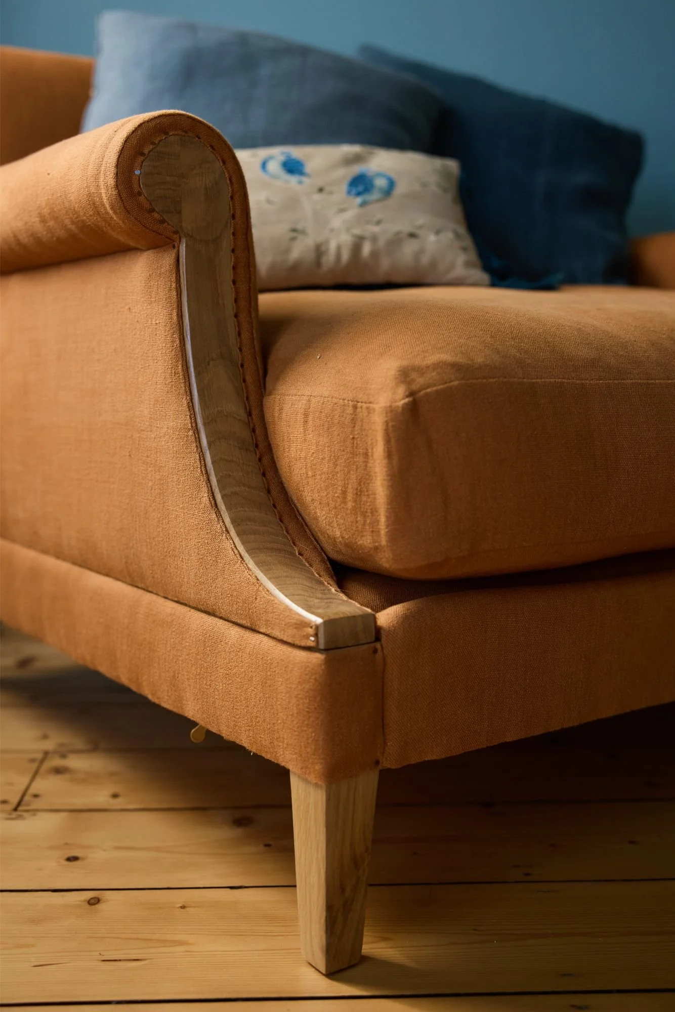 Detail of a hand finished scroll arm on a bespoke large sofa made out of solid oak and upholstered in orange linen styled with blue cushions