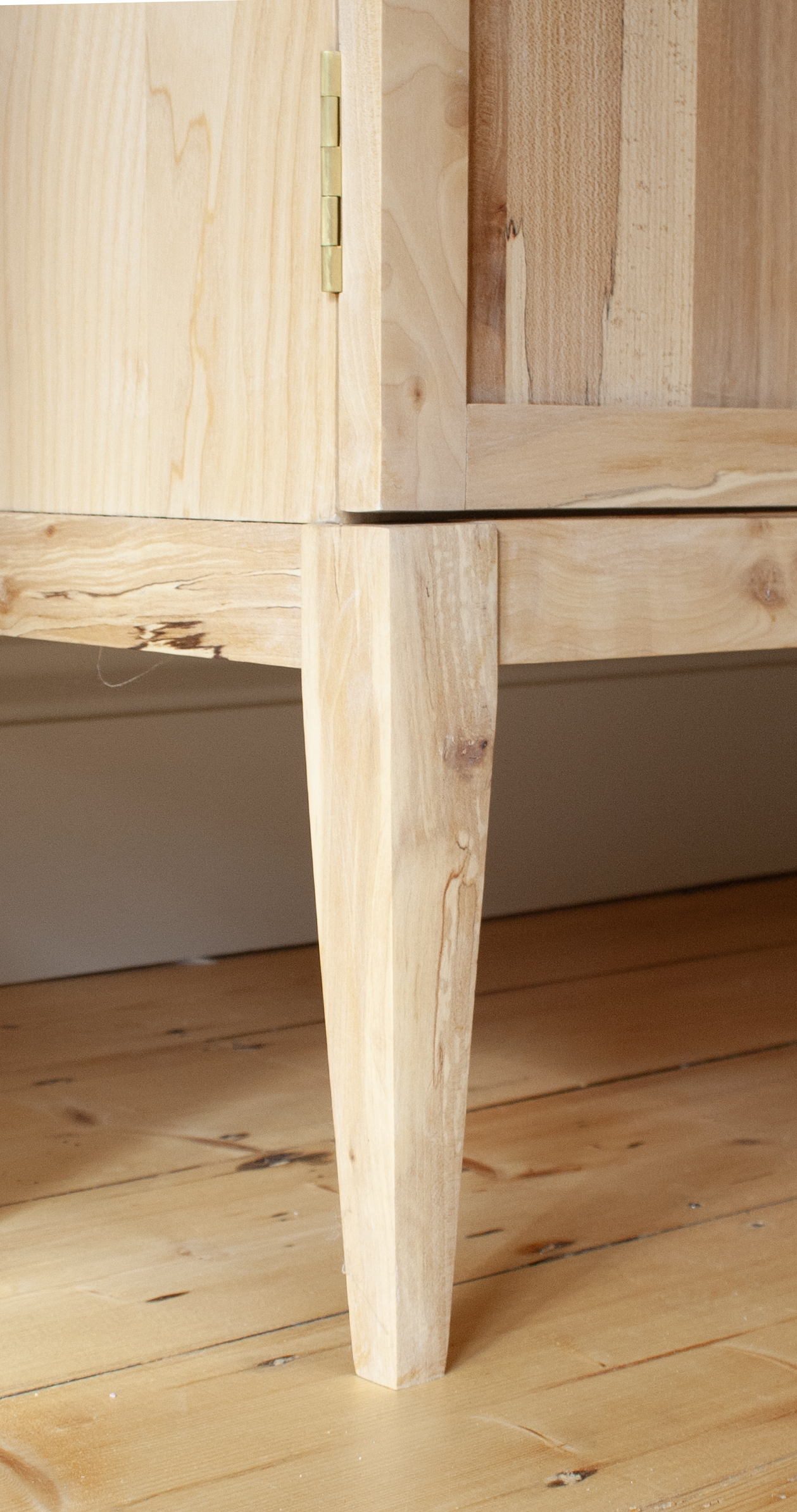 Close-up of a light-colored wooden furniture leg and corner, sitting on a wooden floor.
