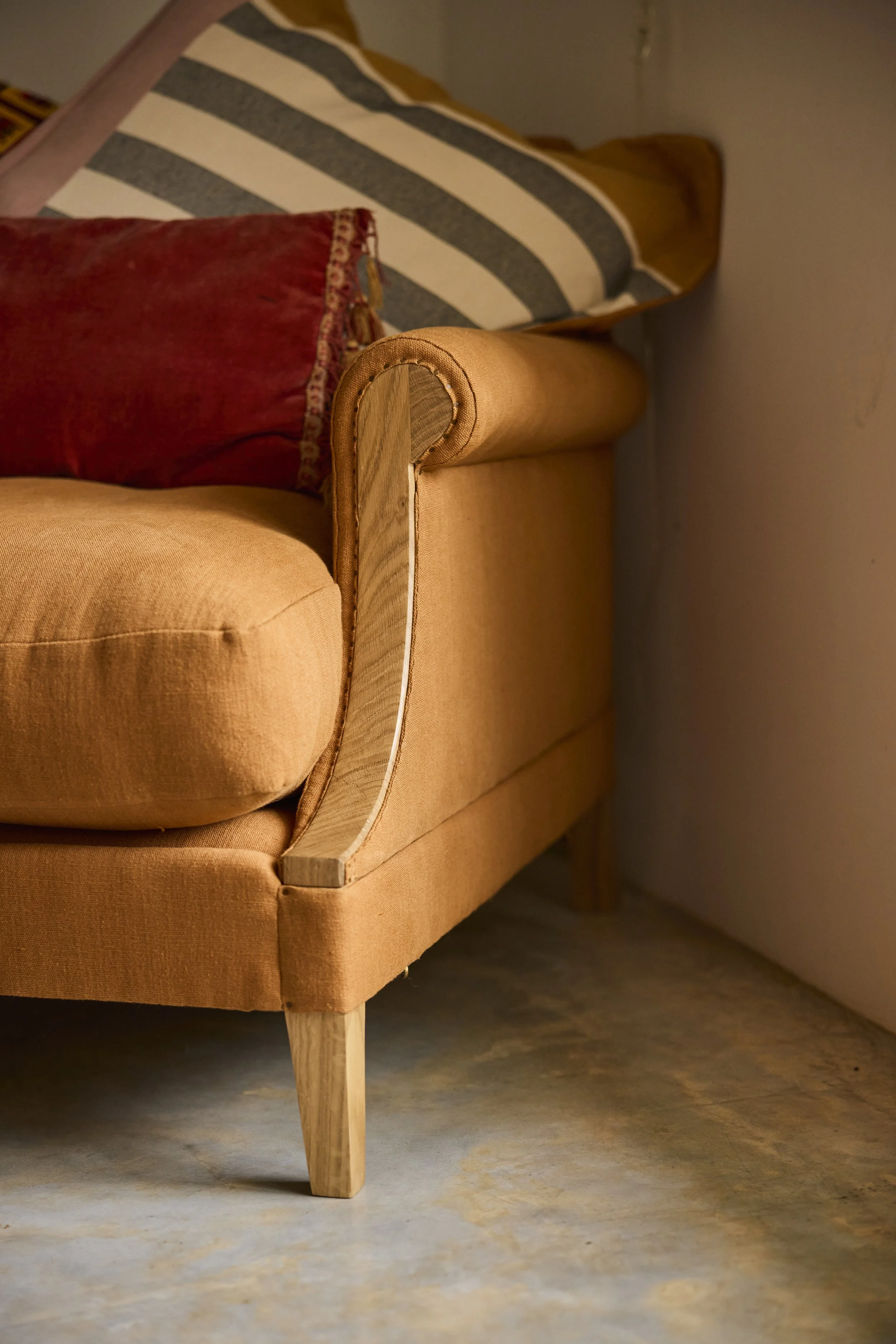 Close-up of a 'brick' coloured Aldan Loveseat seen with exposed oak frame and scroll arms.