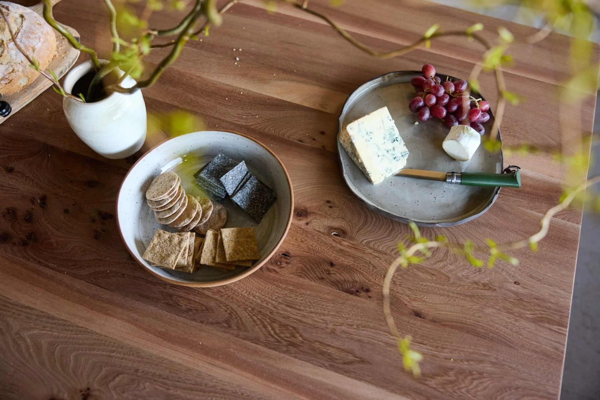 Detail of an elm dining table with varied grain patterns in the dark wood styled with handmade pottery