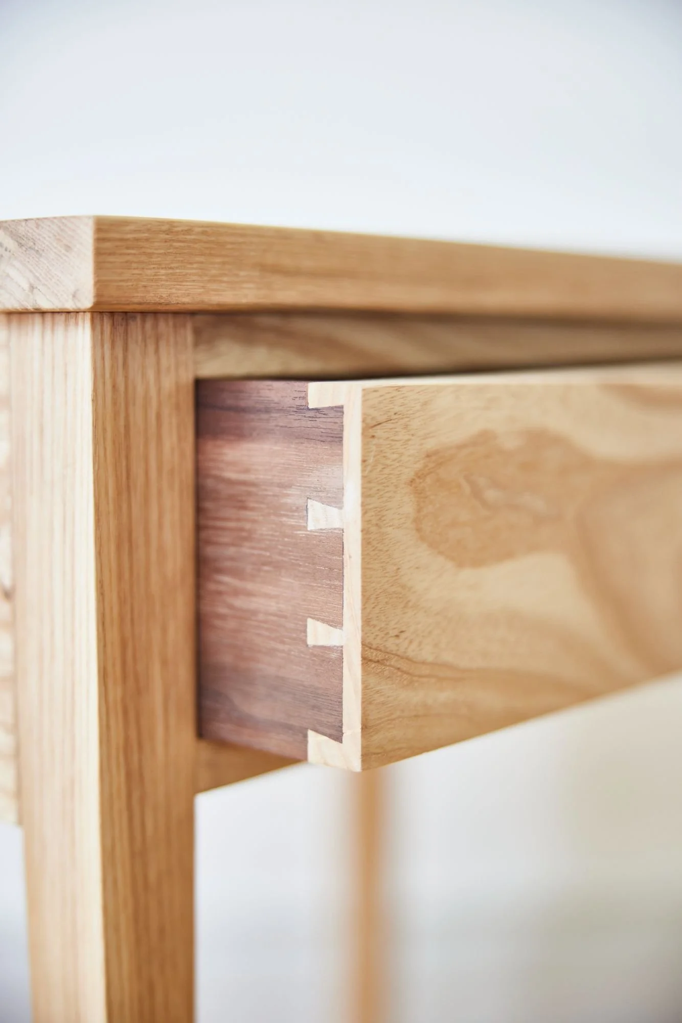 Handcut dovetail detail on a drawer using the contrasting colours of walnut and ash timber. Hand cut by Trew & Bold in their workshop near the Cotswolds