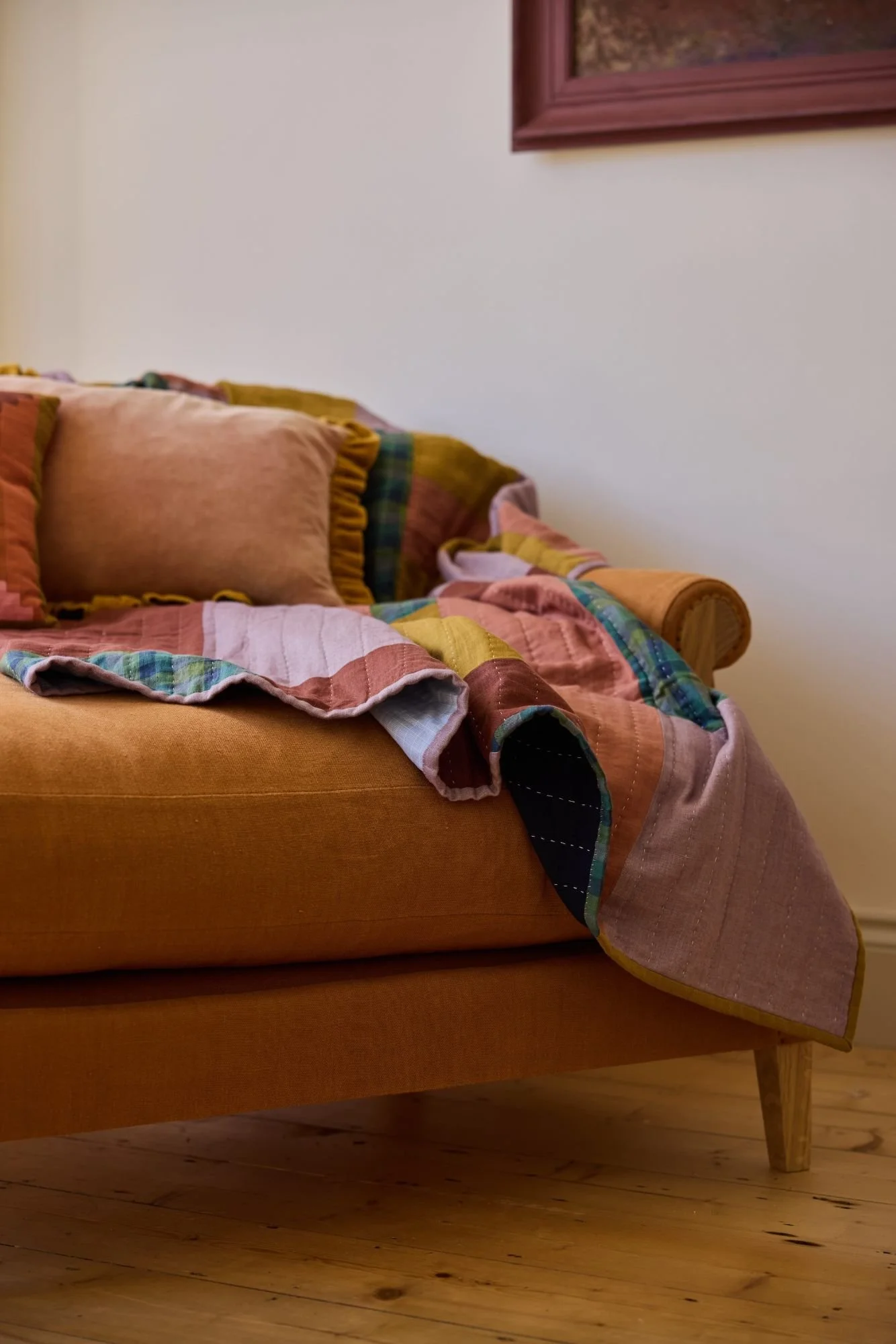 Close up of a large wide and deep comfortable armchair made with solid oak and upholstered in orange linen. Styled with a handmade quilt