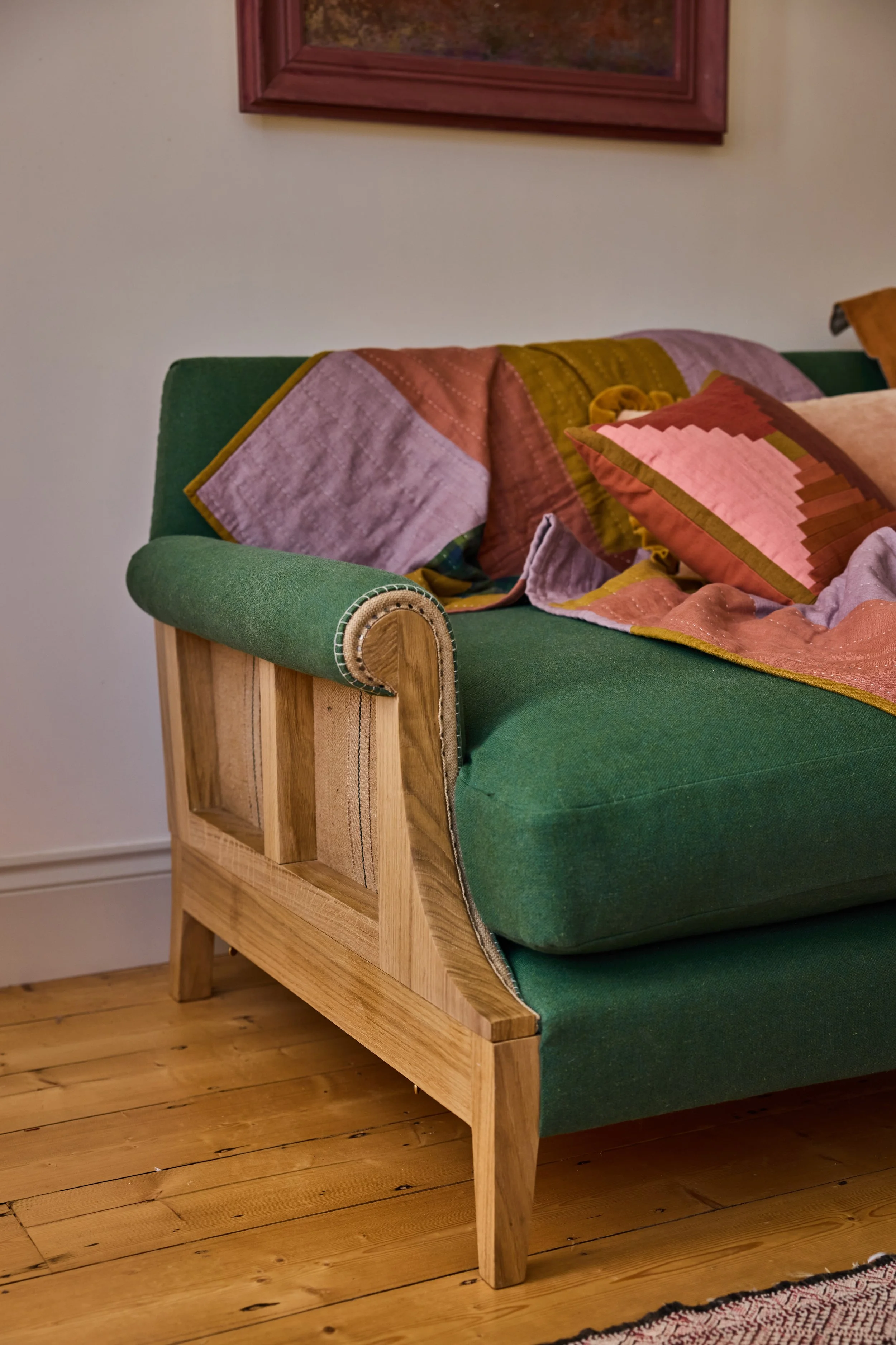 A three quarter view of a solid oak exposed frame sofa where the webbing and hessian of the traditional upholstery are visible with carefully tacked traditional upholstery in a natural wool fabric in green.