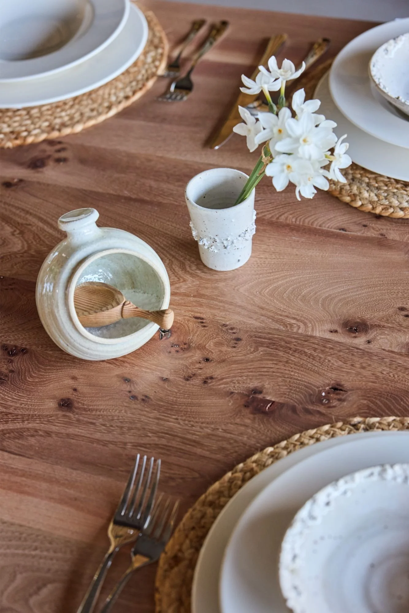 detail of a bespoke elm dining table laid up for a meal with flowers and neutral crockery