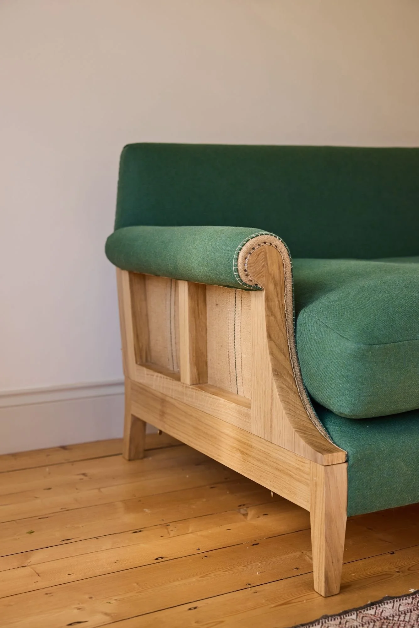 An exposed oak frame on a large sofa where the hessian is exposed finished with traditional upholstery techniques using a green linen and wool fabric