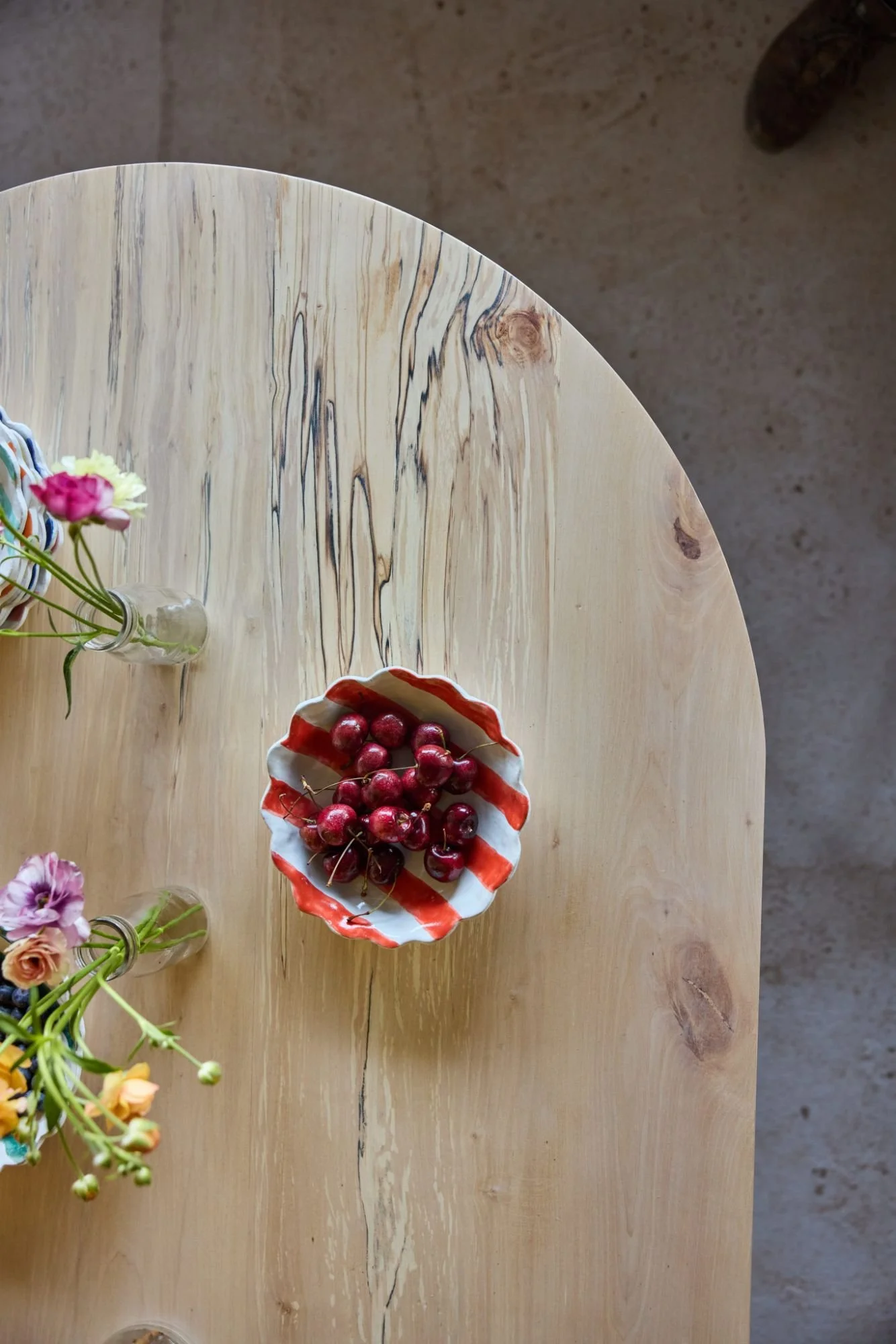 detail of a spalted silver birch curved dining table top styled with bright pottery and fresh fruit
