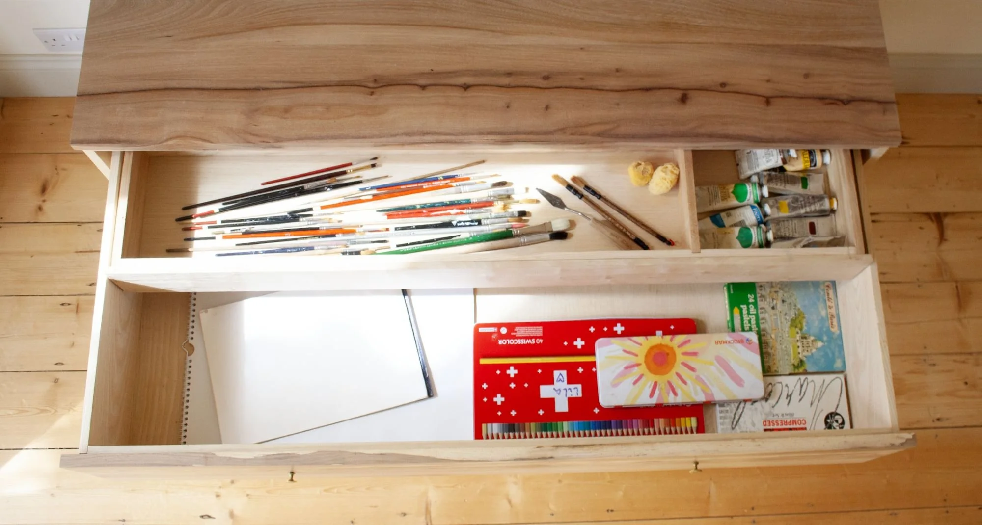 The Thorne Chest of Drawers shows a drawer with art supplies in. Made using solid british timber to meet any client need by Trew & Bold