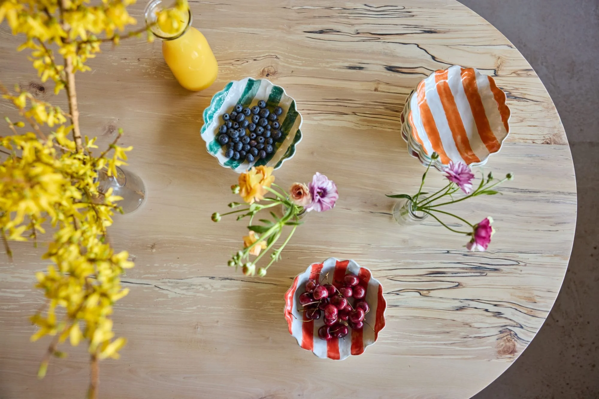 a spring table set up using yellow blossom and bright pottery with fresh fruit on a curved spalted silver birch table top