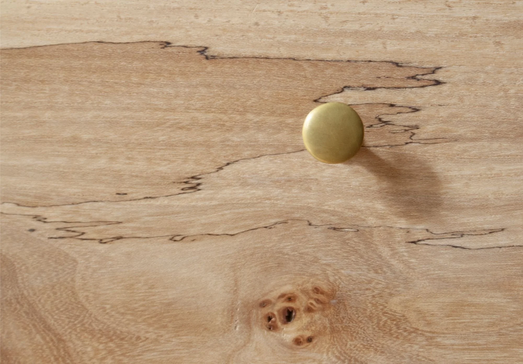Close-up photo of a wooden surface with a brass knob and natural wood knots and grain.