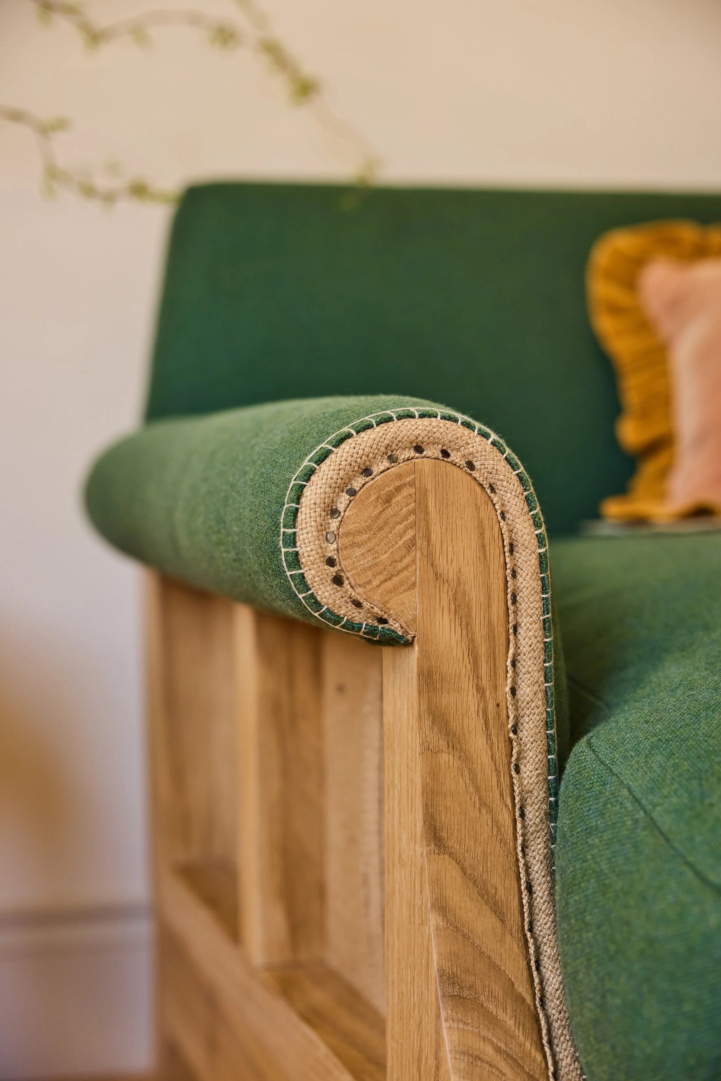 Detail of the scroll arm of a handmade sofa, with hand spokeshaved arms and traditionally upholstered using steel tacks with visible hessian and blanket stitch details on the front of the arm. Designed to be unique
