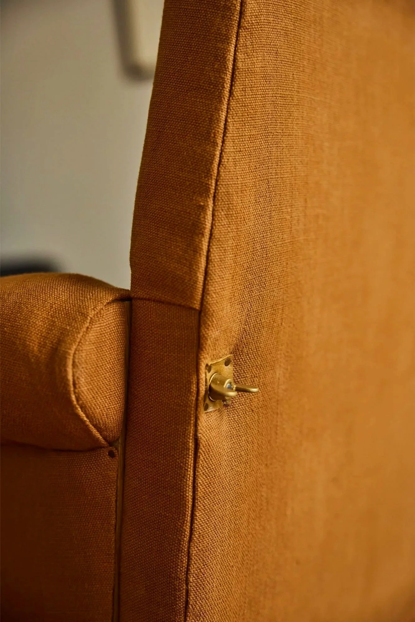 detail of brass hardware on the back of a bespoke loveseat that you can take apart to easily move all covered in orange linen